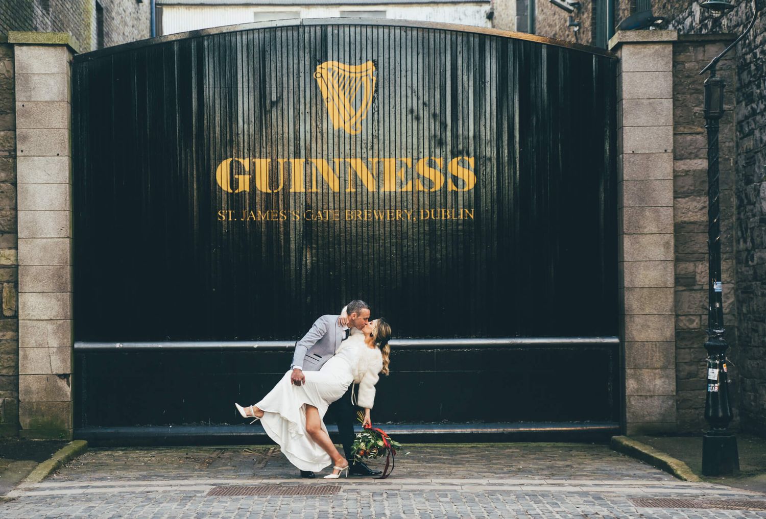 Bride and groom share a dramatic dipped kiss in front of the black Guinness Storehouse gate in Dublin photo by AK wedding photography