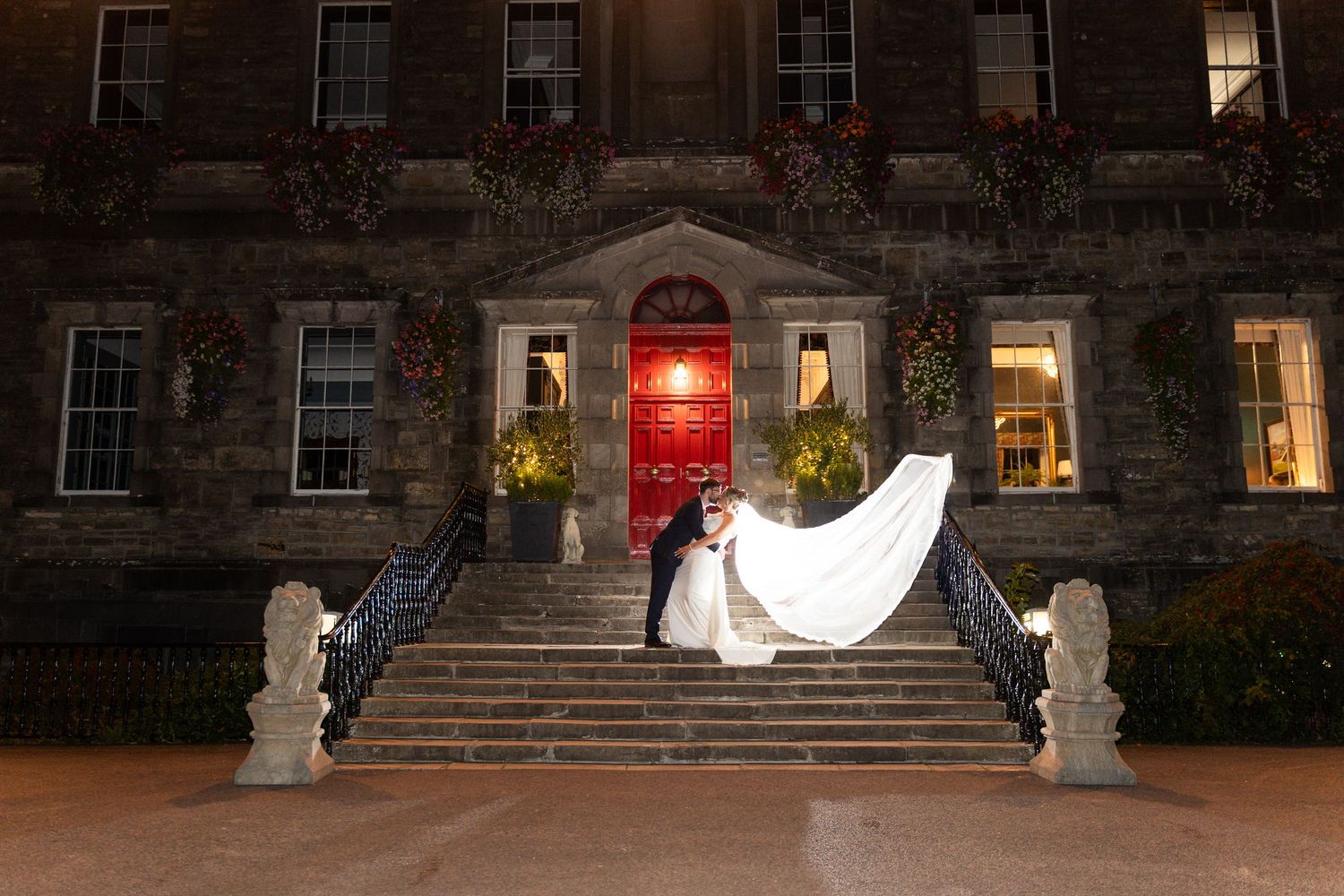 Bride and groom share a romantic kiss on grand stone steps of Bellinter house at night, wedding veil flowing dramatically.