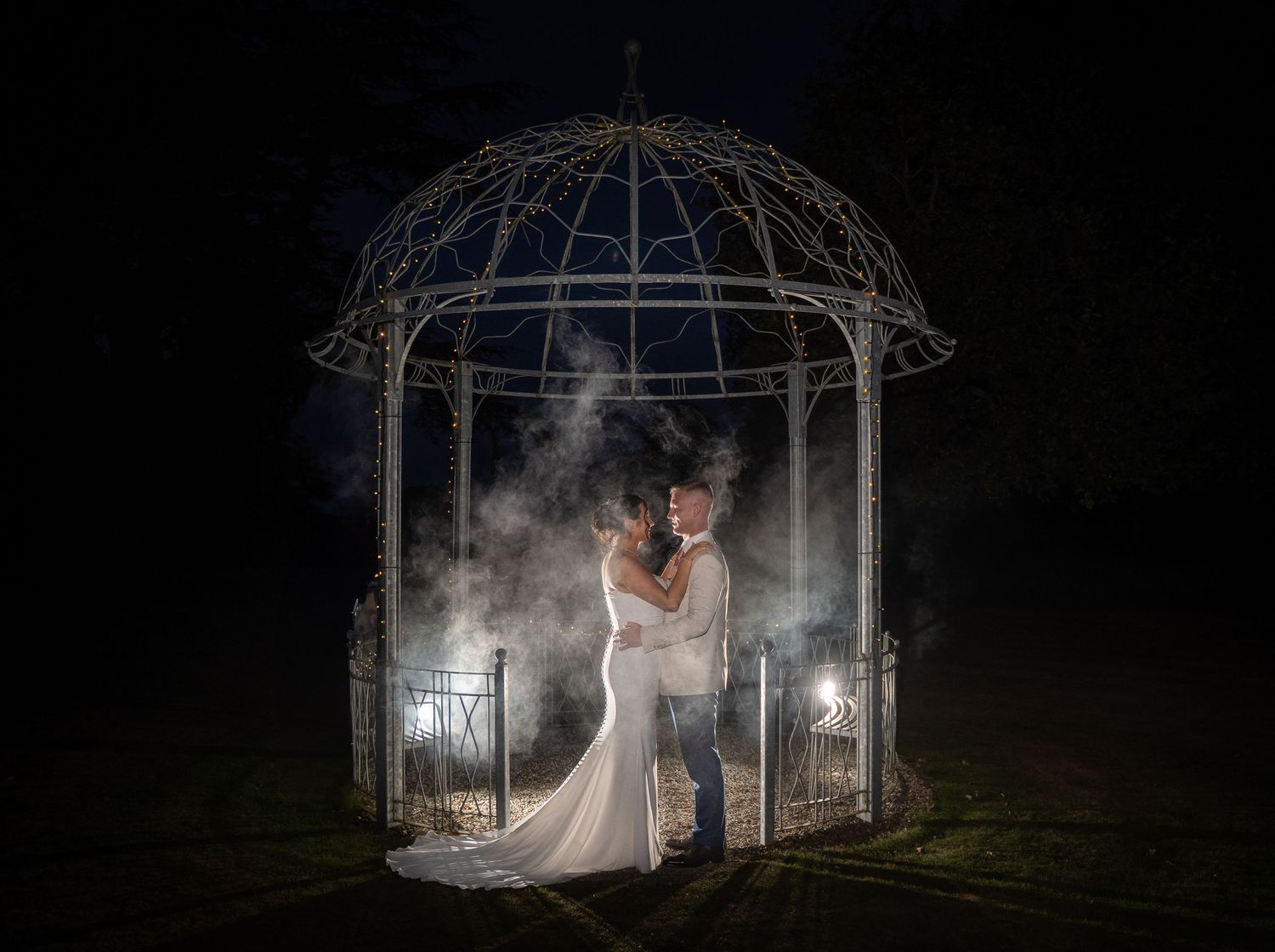 A romantic wedding photo series showing a couple in a glowing gazebo at night surrounded by ethereal fog and lighting.