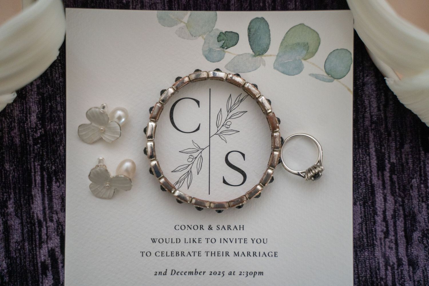 Silver wedding jewelry and pearl earrings displayed on a Conor and Sarah wedding invitation dated 2nd December 2023.