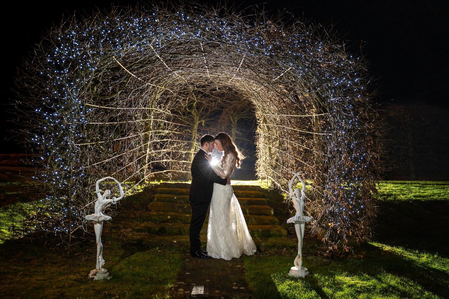 Bride and groom embrace at night inside a  fairy-light tunnel at Ballymagarvey village photo by AK wedding photography and videography.