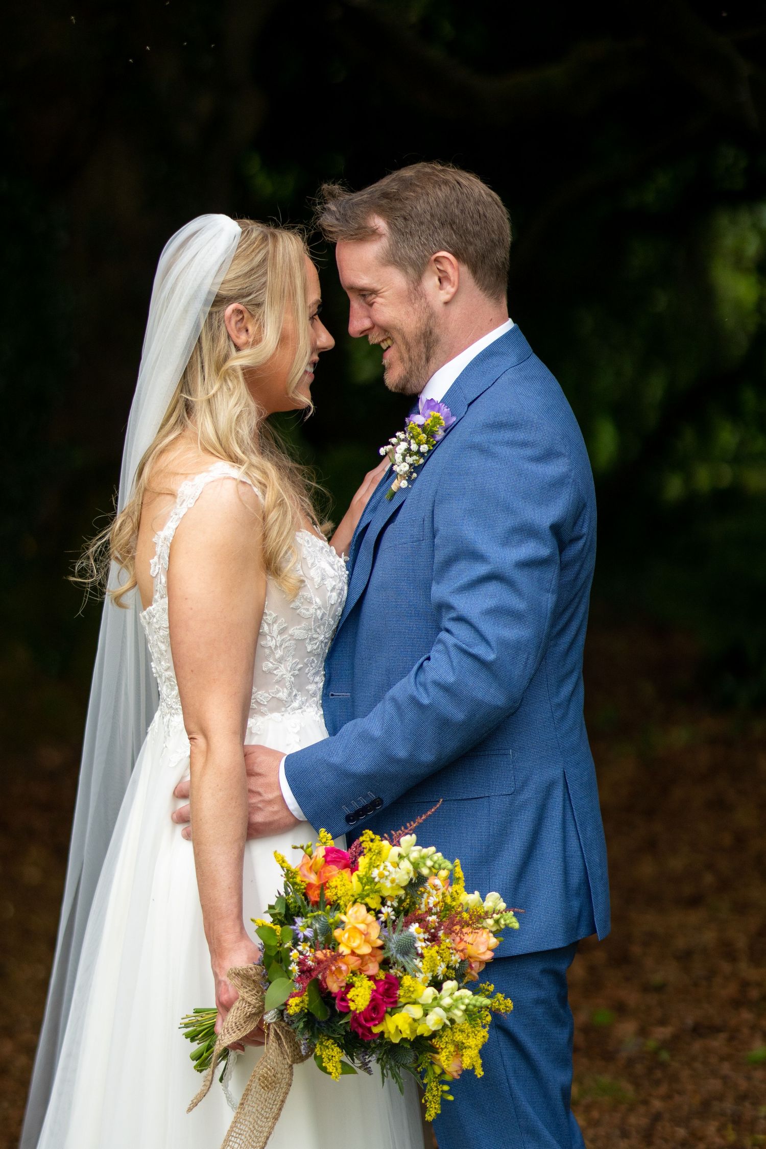 Bride and groom share a joyful moment, holding a colorful bouquet, dressed in white gown and blue suit at Bellinter house.