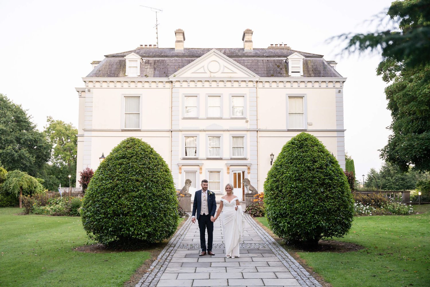 Bride and groom walk hand in hand along a stone path toward Moyvalley house - photo by AK wedding photography and videography.