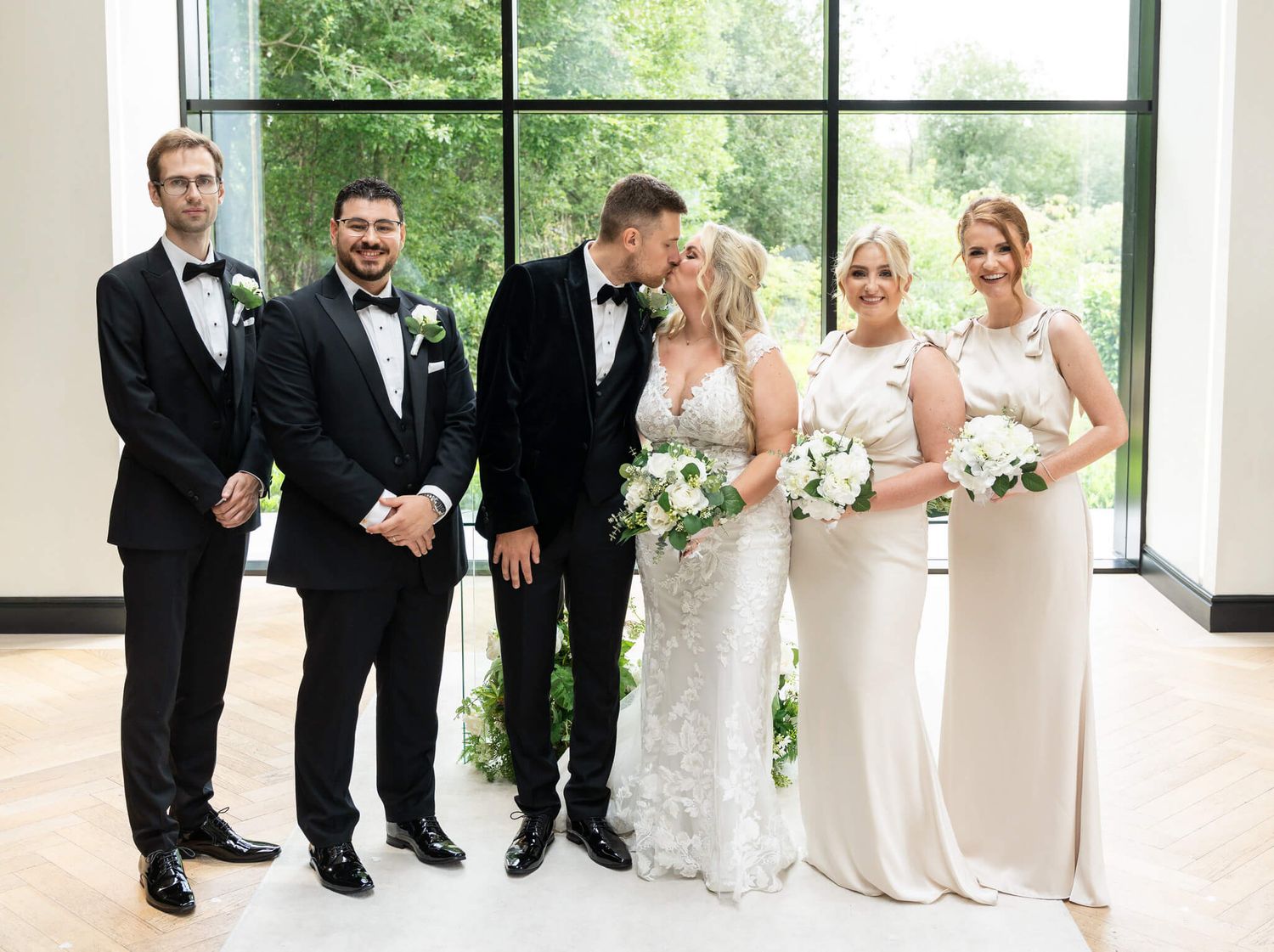 Groom kisses bride's cheek with bridal party at Cabra Castle County Cavan - photo by AK wedding photography and videography.
