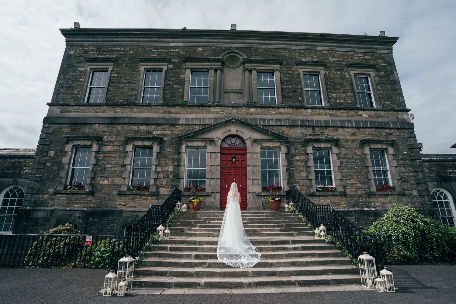 Bride in white gown with long veil on steps of historic stone wedding venue with red door at Bellinter house.