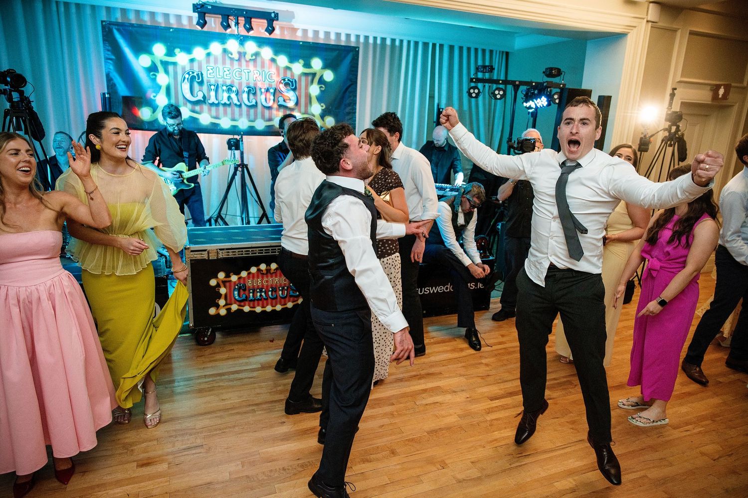 Guests dancing energetically at a circus-themed party in a decorated ballroom with colorful lights.