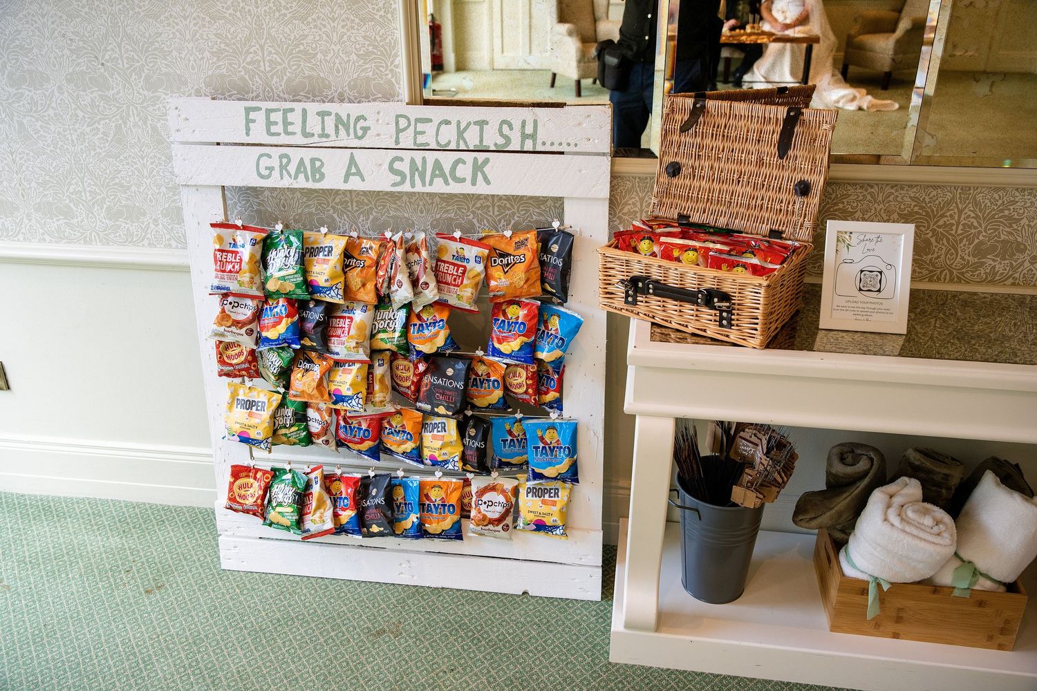 A creative snack station display board with colorful chip bags arranged neatly, featuring a sign reading Feeling Peckish Grab a Snack.