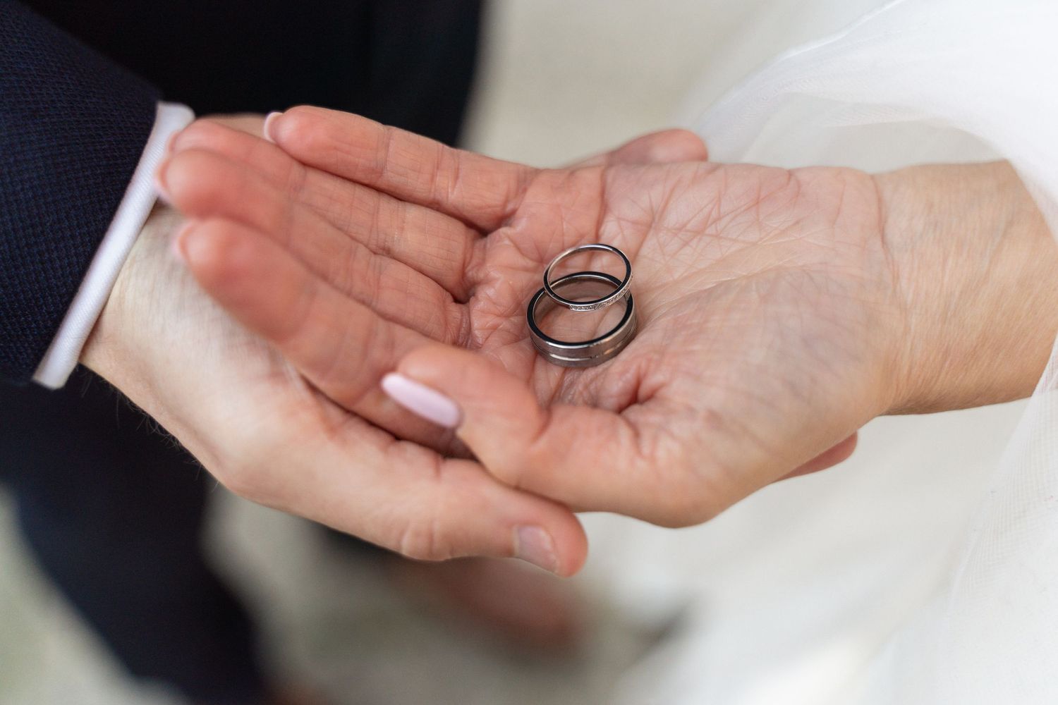 Two hands holding silver wedding rings on a palm, symbolizing marriage and commitment.