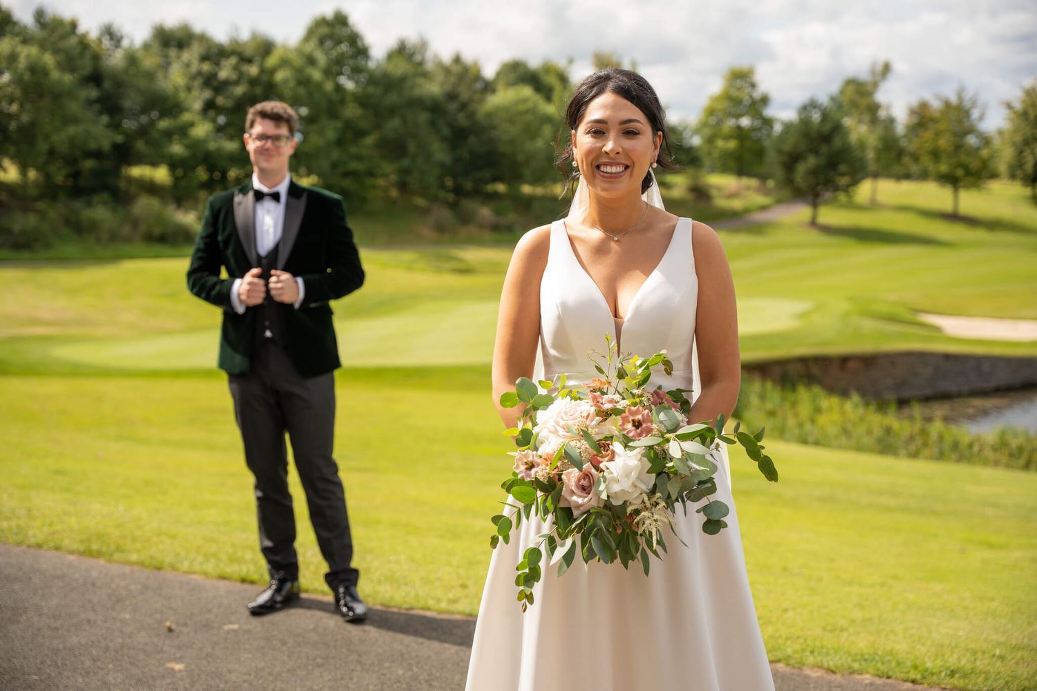 Smiling bride holds a floral bouquet while the groom in stands behind her at the Heritage hotel photo by AK wedding photography and video
