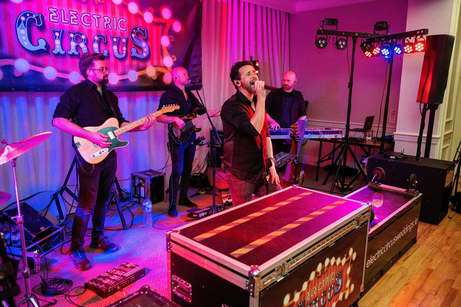 Live band performing on stage at Electric Circus venue with guitarist, vocalist, and keyboardist under colorful stage lighting.