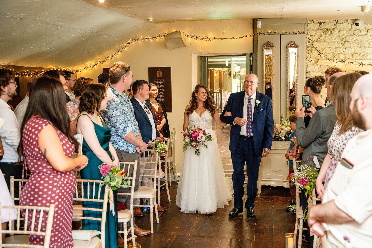 Bride in a white gown holding a pink bouquet walks down the aisle with her father at The Anglers Rest photo by AK wedding photography.