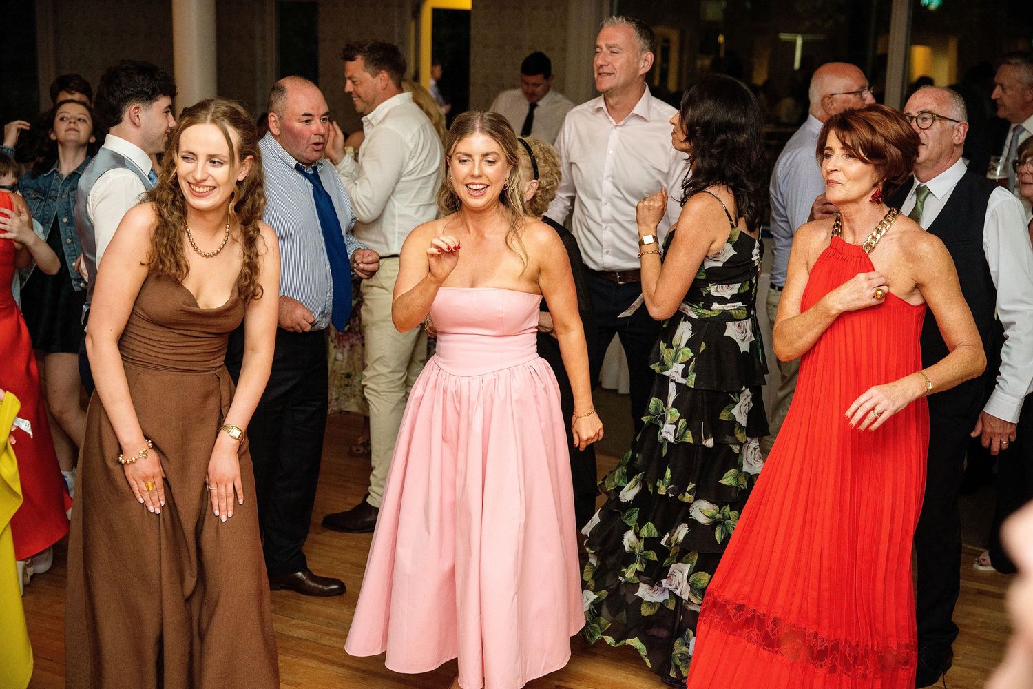 Women in elegant dresses dancing joyfully at a formal wedding reception party on a dance floor.
