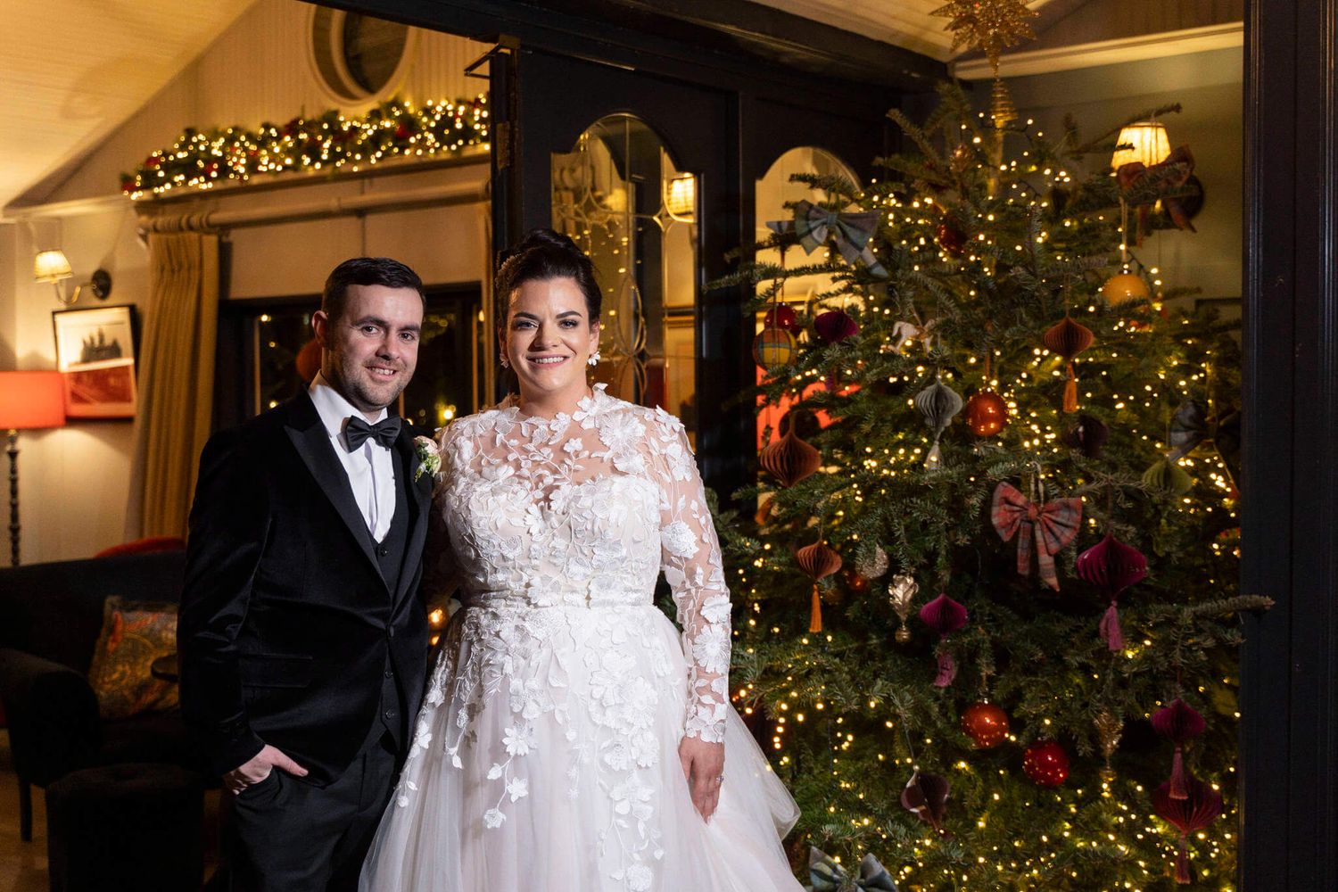 Bride and groom pose beside a Christmas tree at a winter wedding the StationHouse Kilmessan photo by AK wedding photography and videography.