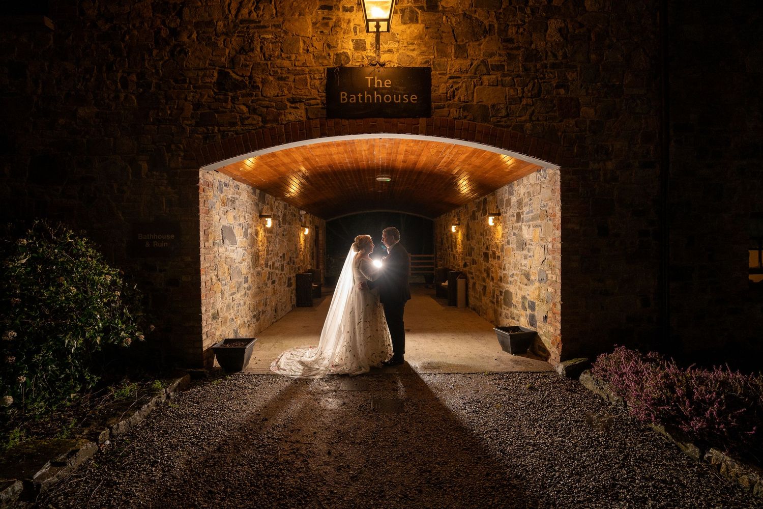Bride and groom silhouetted in a romantic stone archway at Bellinter house illuminated by warm golden lights at night.