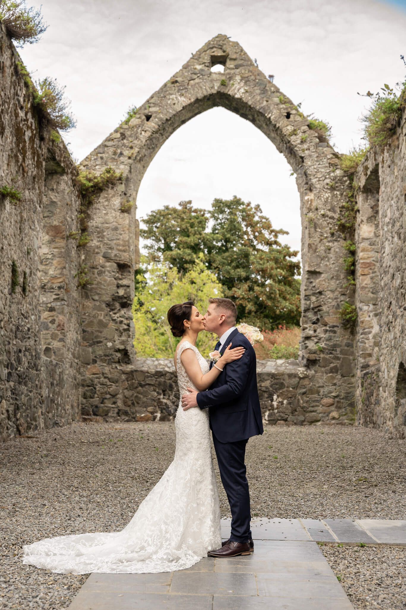 Bride kisses groom beneath a stone arch in the ruins of an old abbey Carlingford county Louth photo by AK wedding photography & Videography.
