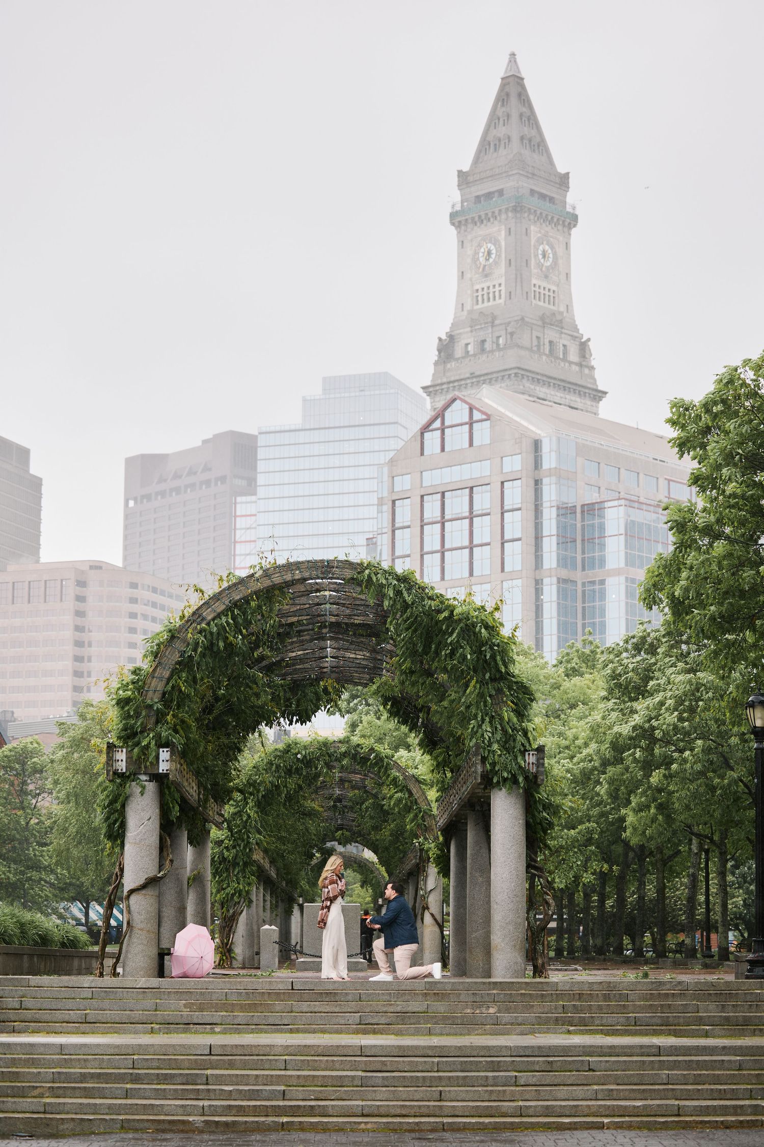 Couple's proposal under ivy-covered arches at Christopher Columbus Park, Boston, with Custom House Tower backdrop.