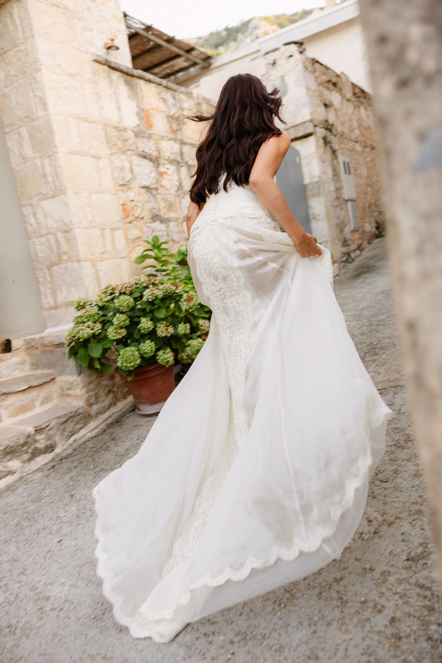 Bride in flowing white dress walking along stone pathway. Hvar, Croatia