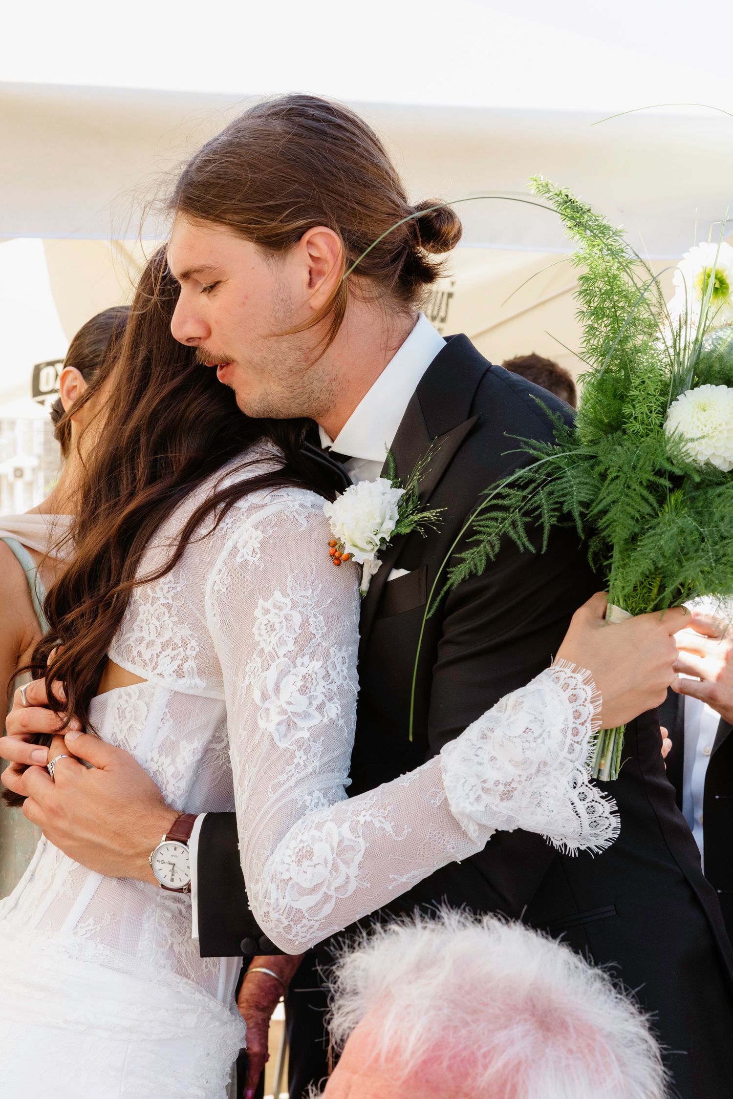 Intimate embrace between newlyweds with fern bouquet during wedding ceremony.
