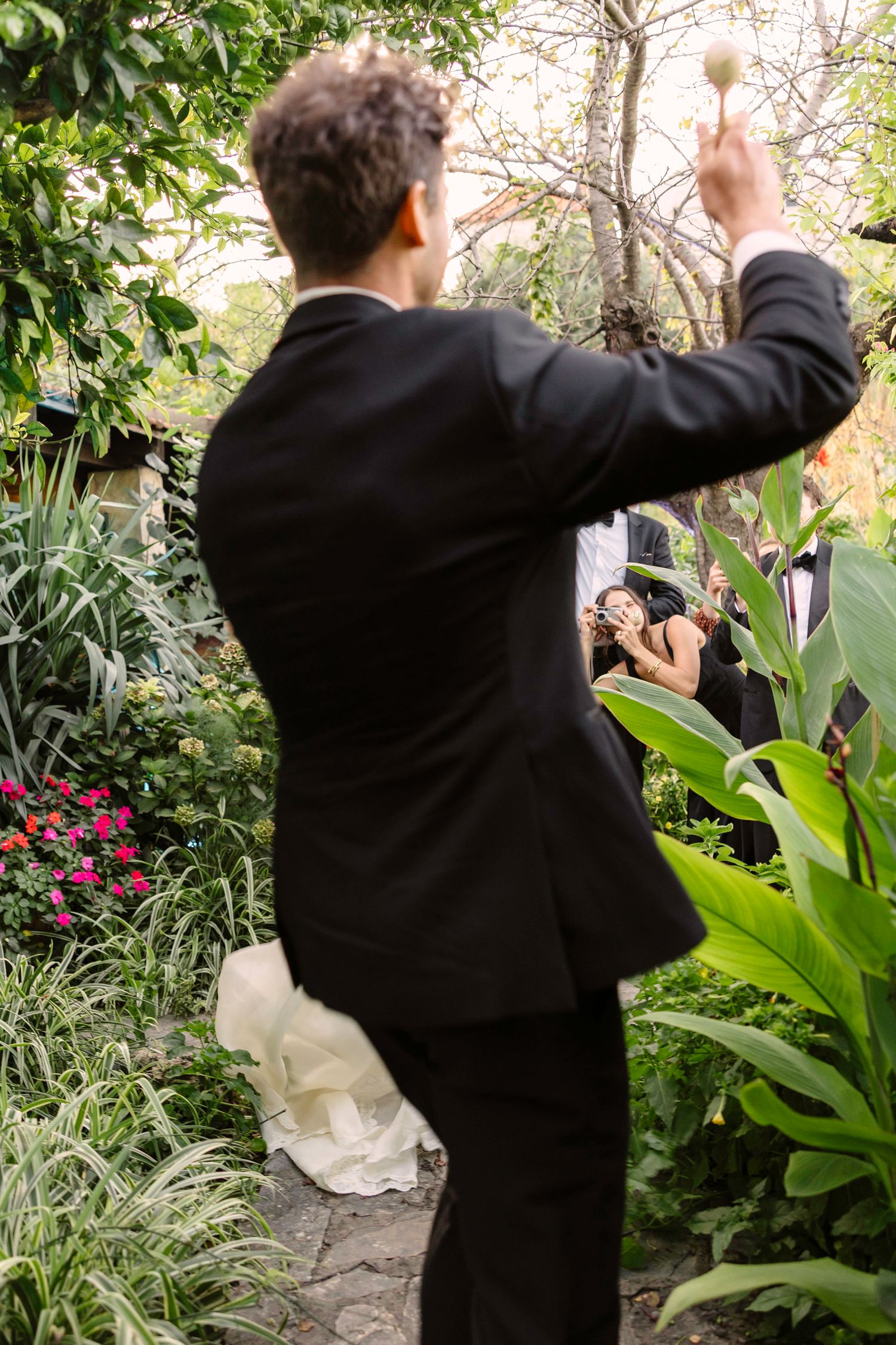 Guest in formal attire raises a glass in celebration among garden greenery at outdoor wedding. Hvar, Croatia