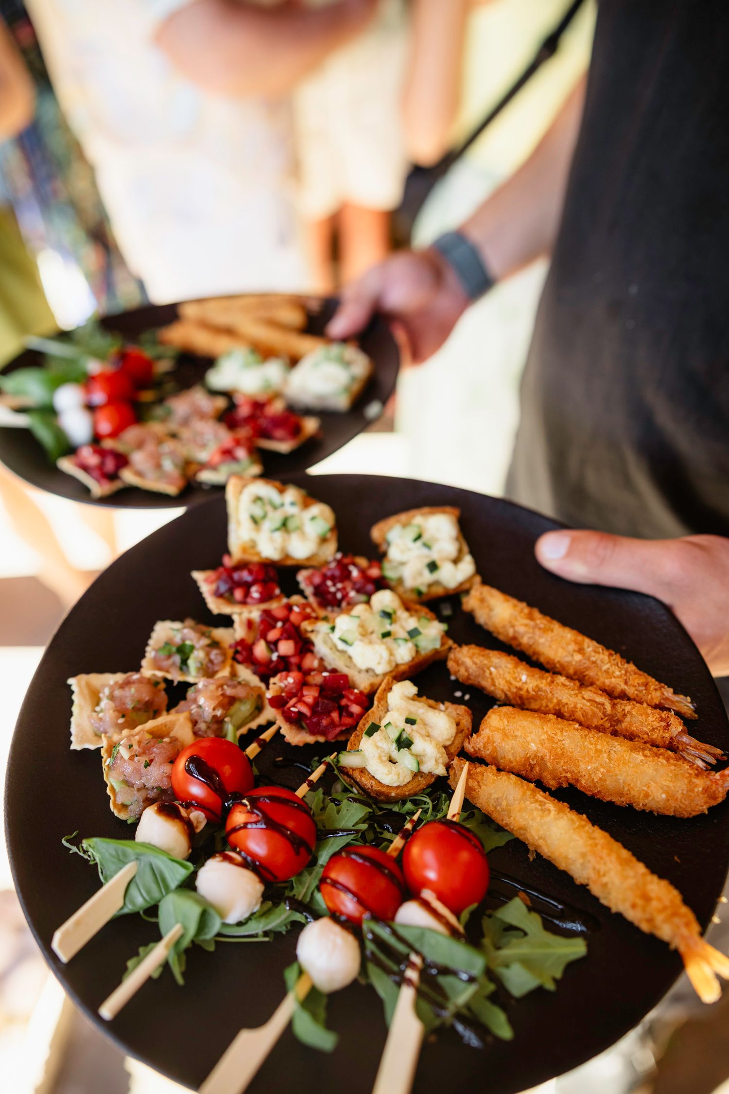 Appetizer plate with grilled shrimp skewers, cherry tomatoes, and breadsticks on dark plate.