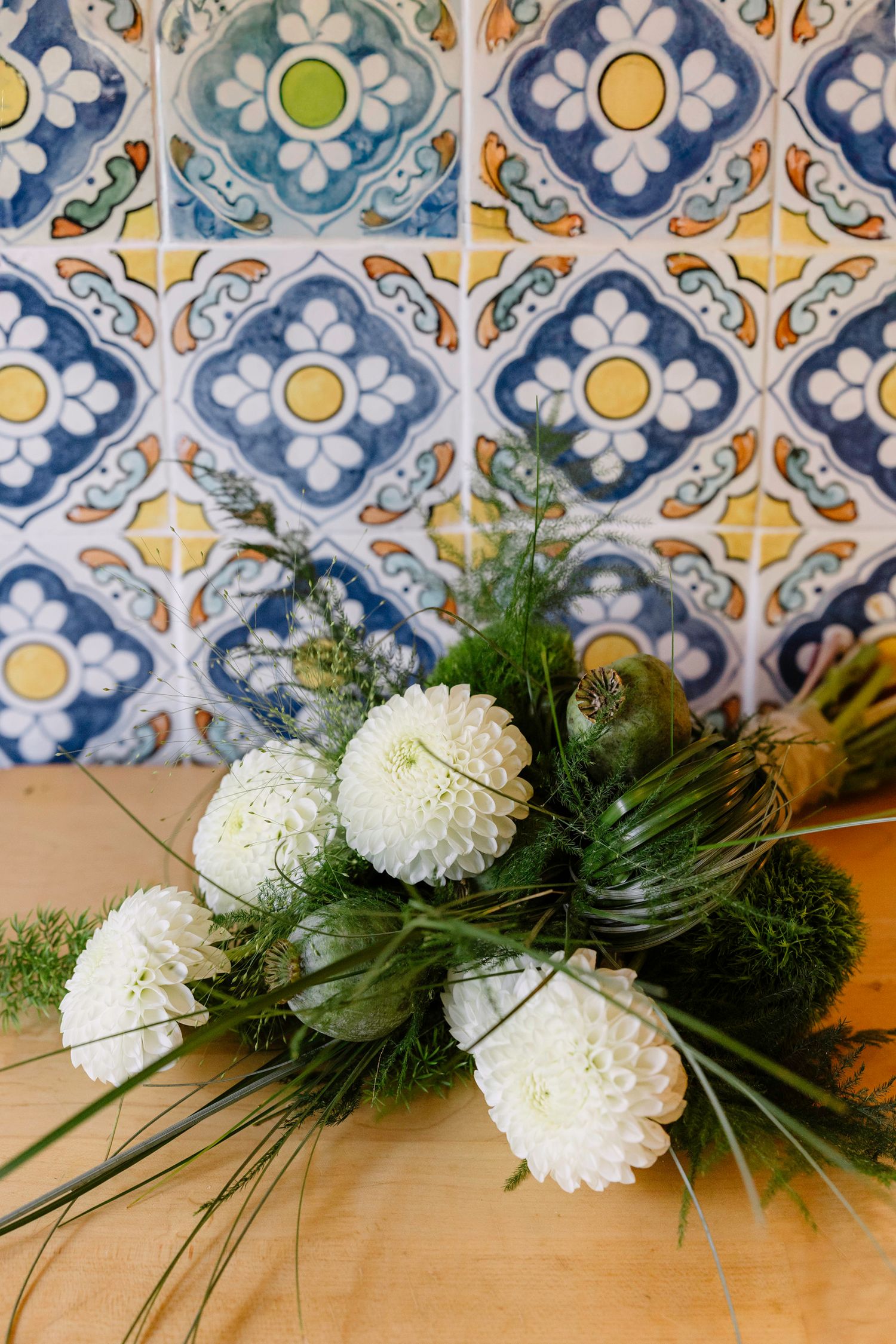 White carnations and greenery arrangement against blue and yellow patterned tile background.