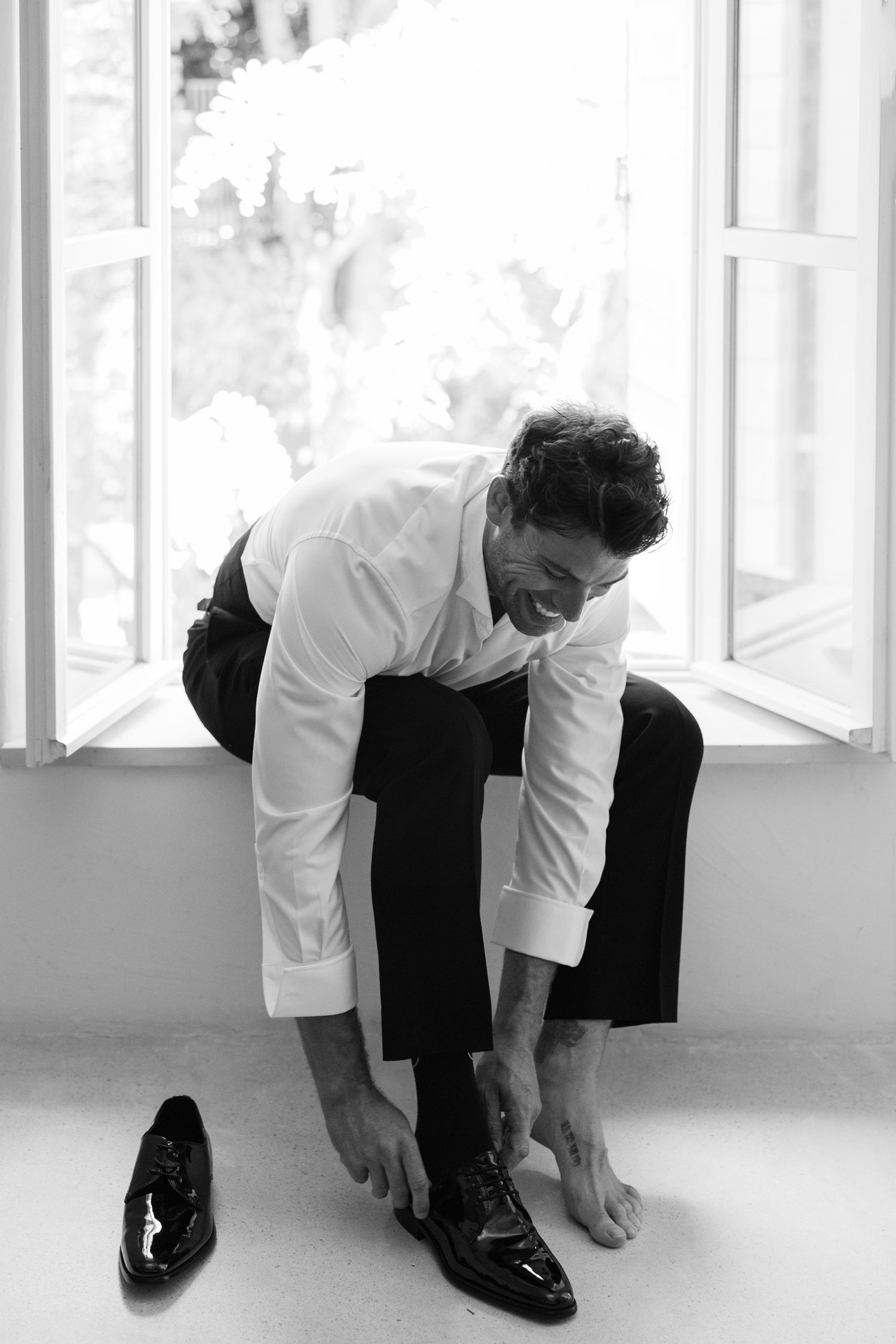 Black and white image of someone adjusting formal shoes while getting dressed.
