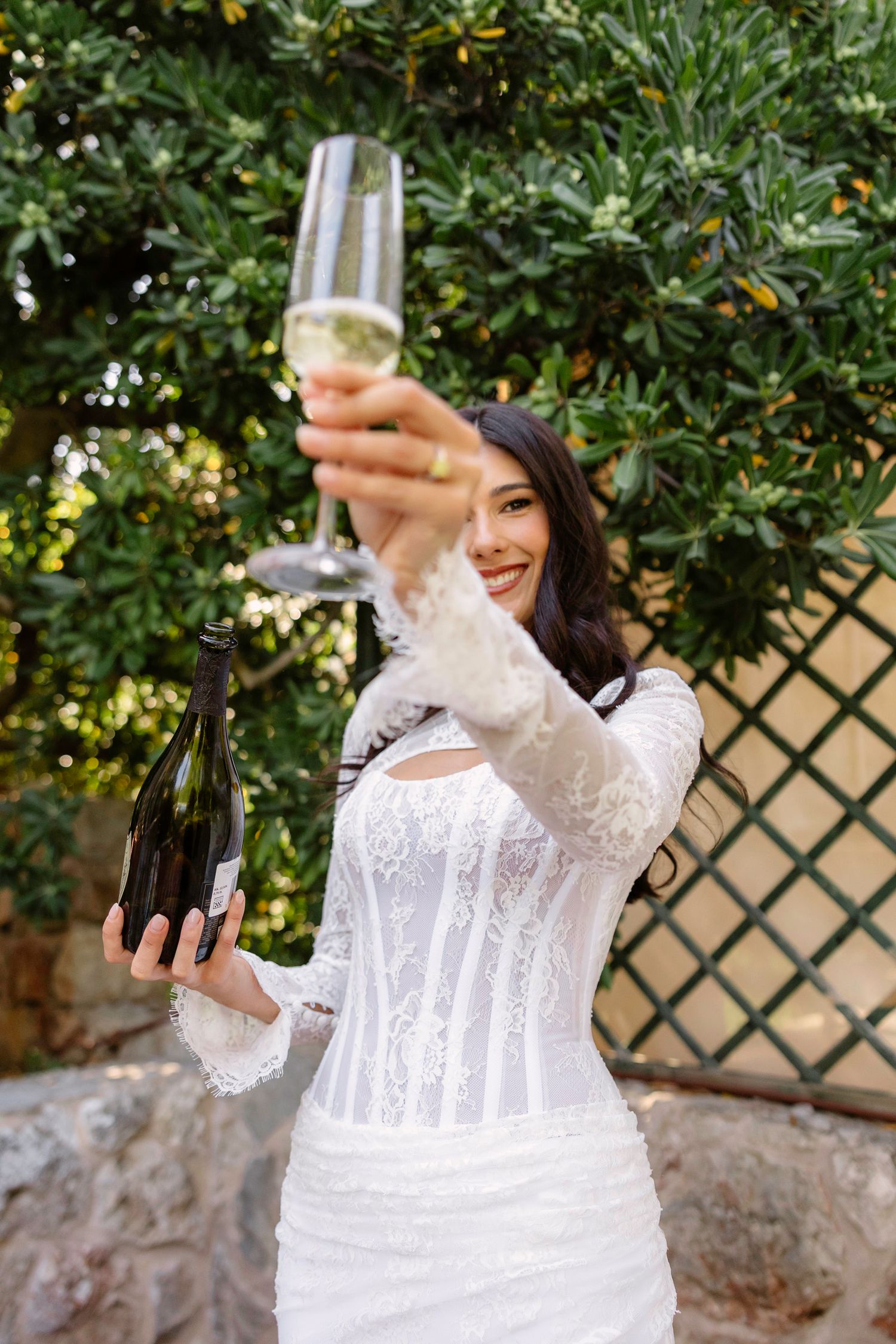 A white lace wedding dress is shown in detail against a garden backdrop.
