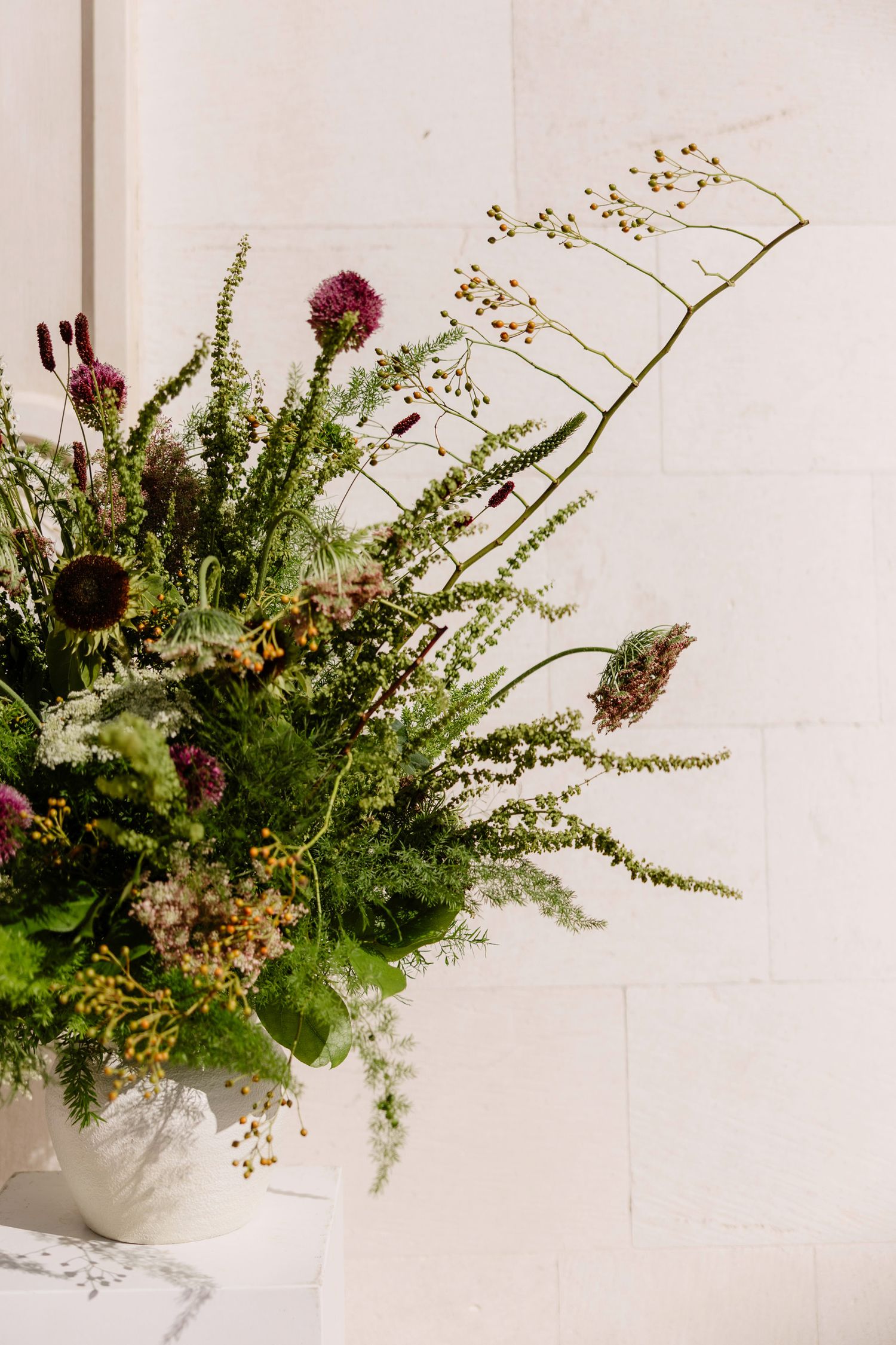 Artistic floral arrangements with ferns and purple blooms in white vases.