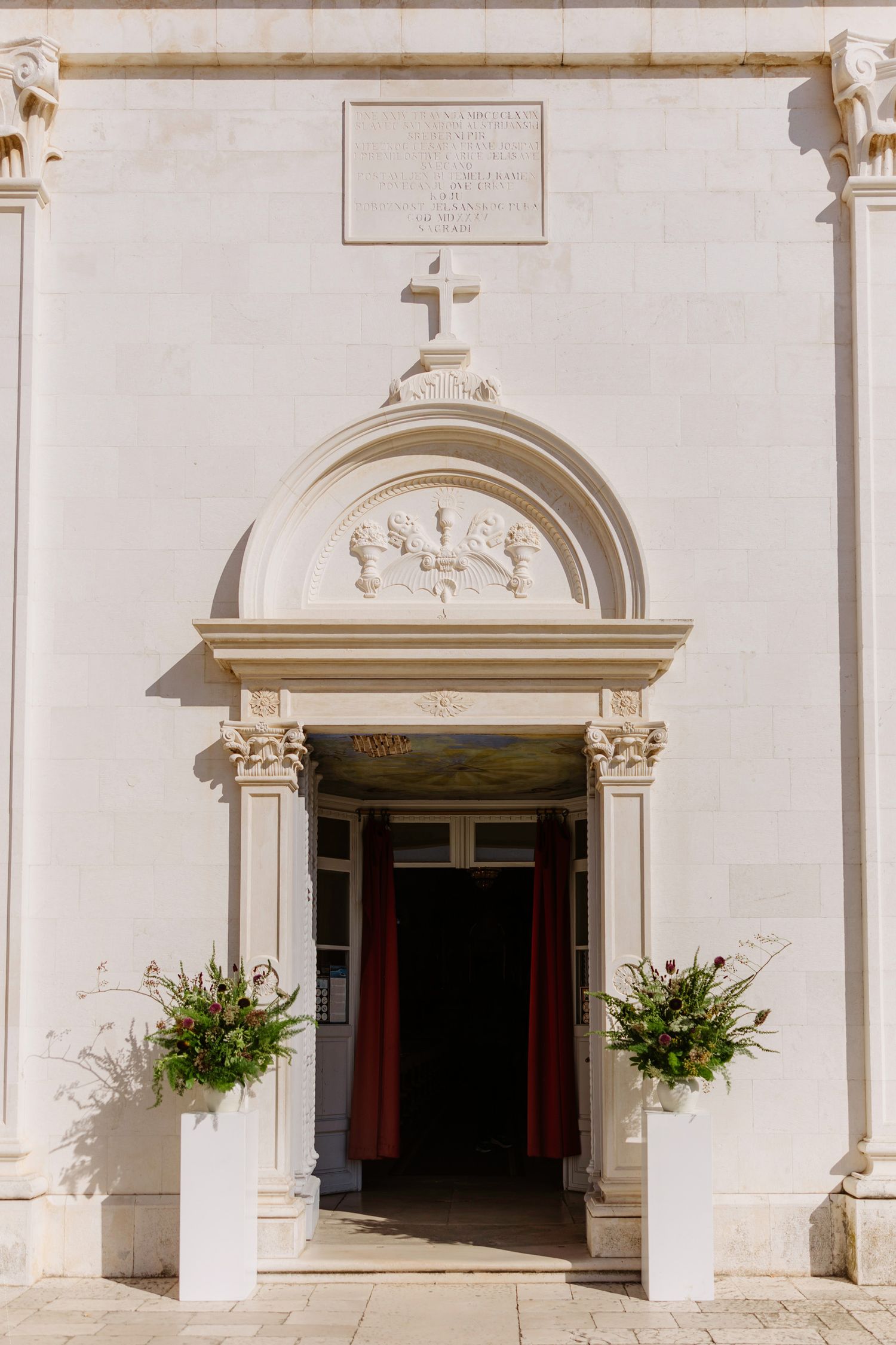 Elegant white church entrance with ornate architectural details and hanging floral arrangements.