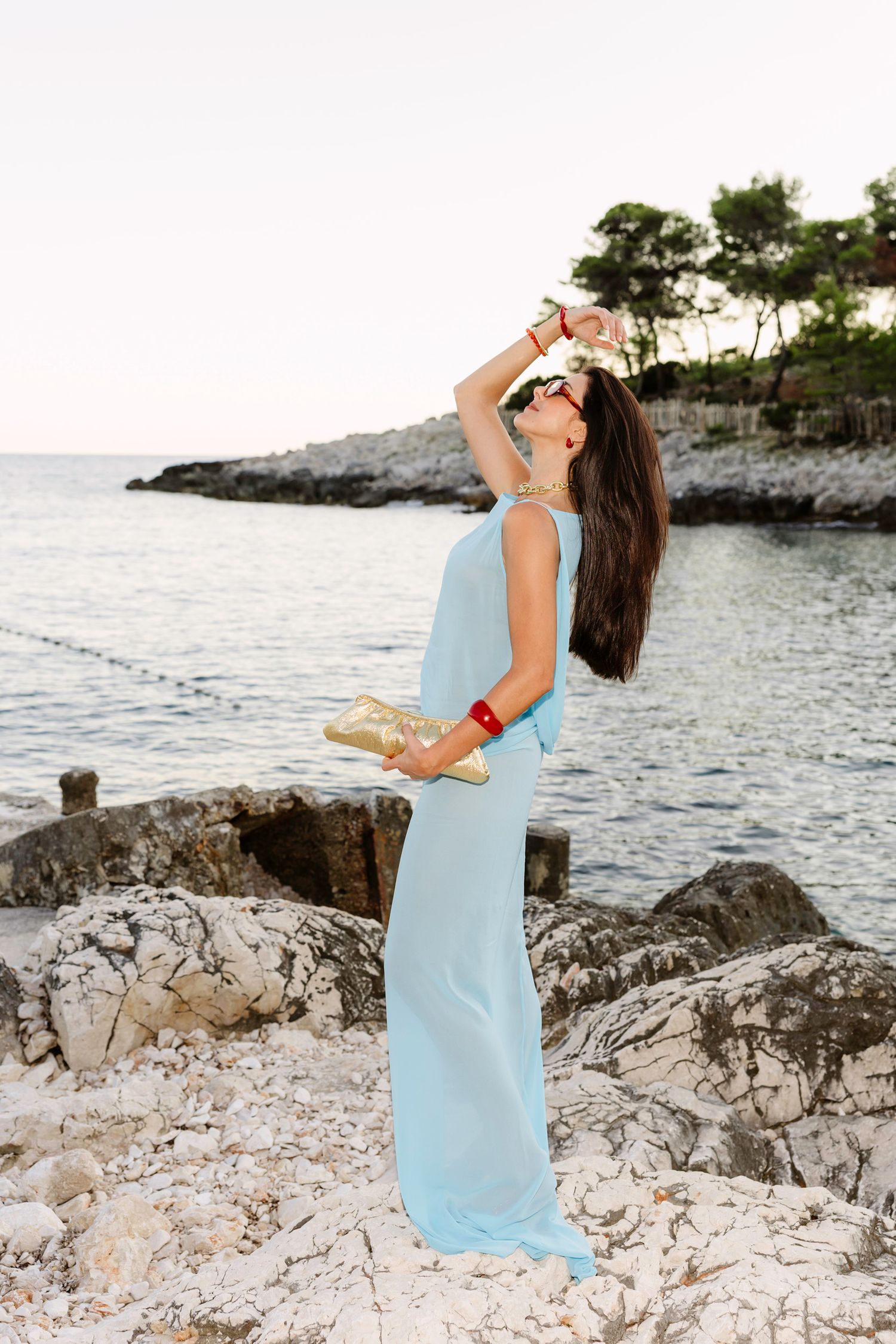 A woman in a light blue dress poses gracefully on white limestone rocks by the ocean.