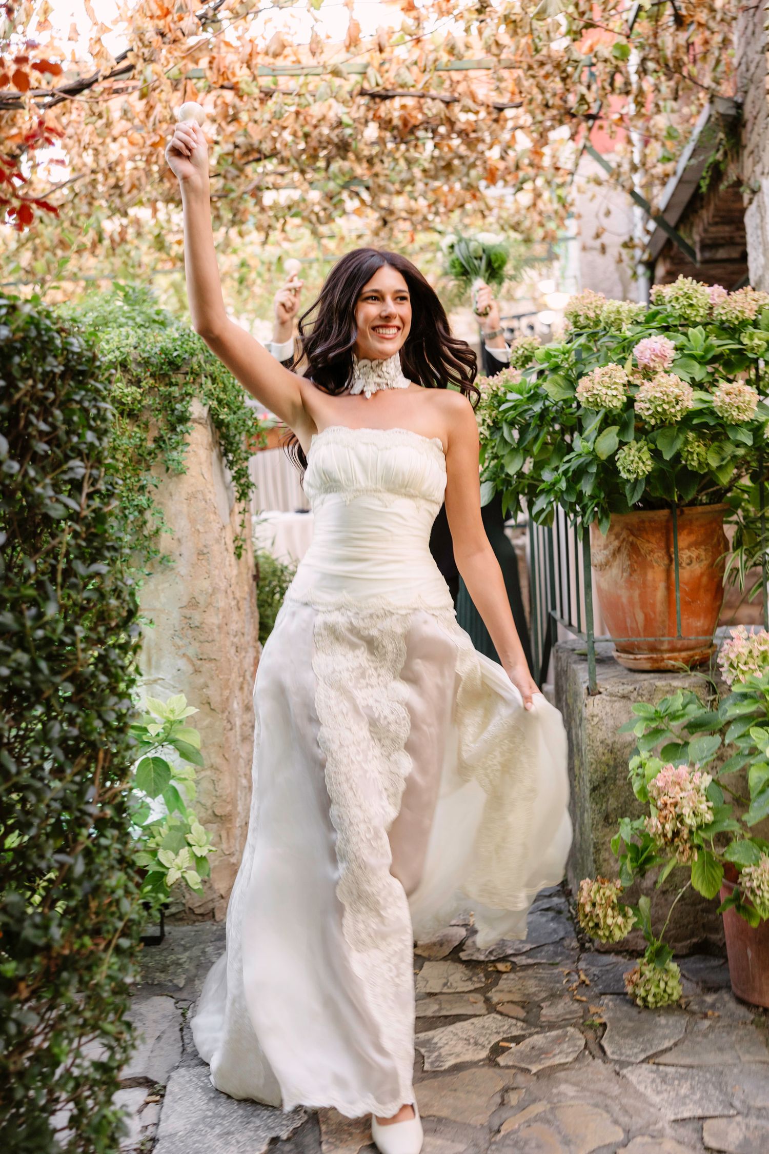 A bride in a stunning white lace gown celebrates joyfully in a garden setting with blooming flowers. Hvar, Croatia