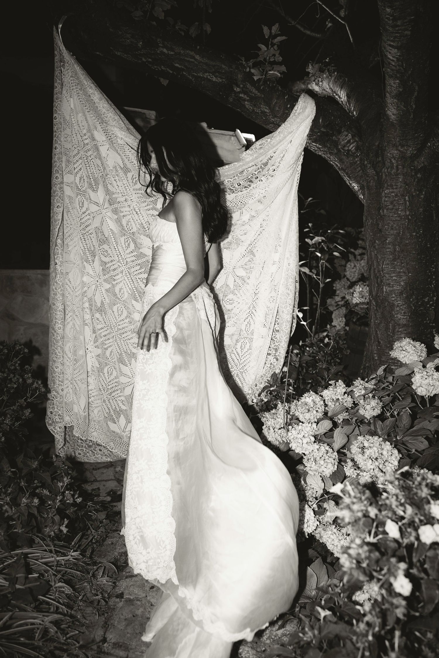 Black and white photos of a bride in a lace dress posing near garden flowers at night. Hvar, Croatia