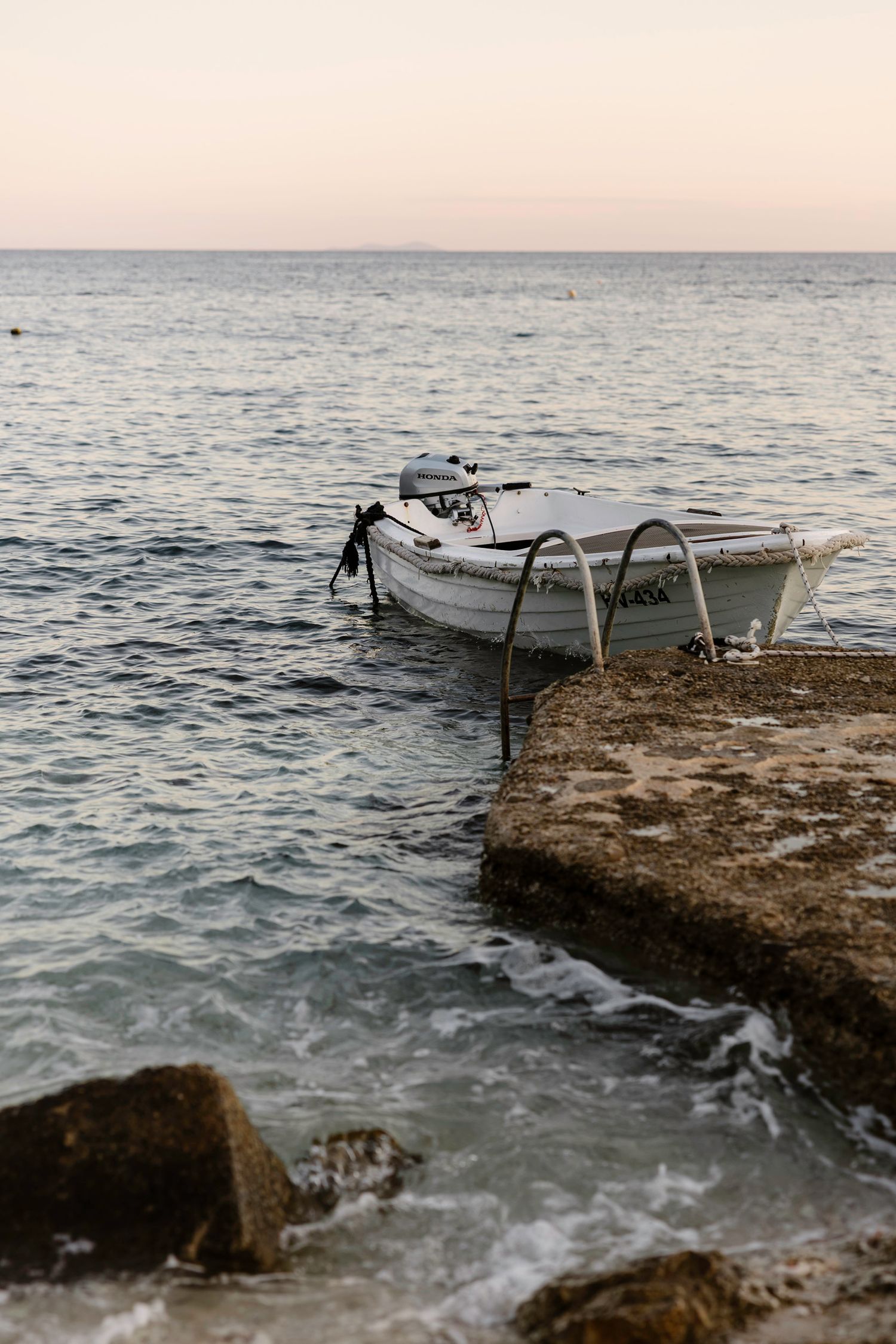 Small white boats moored near rocky coastline during sunset.