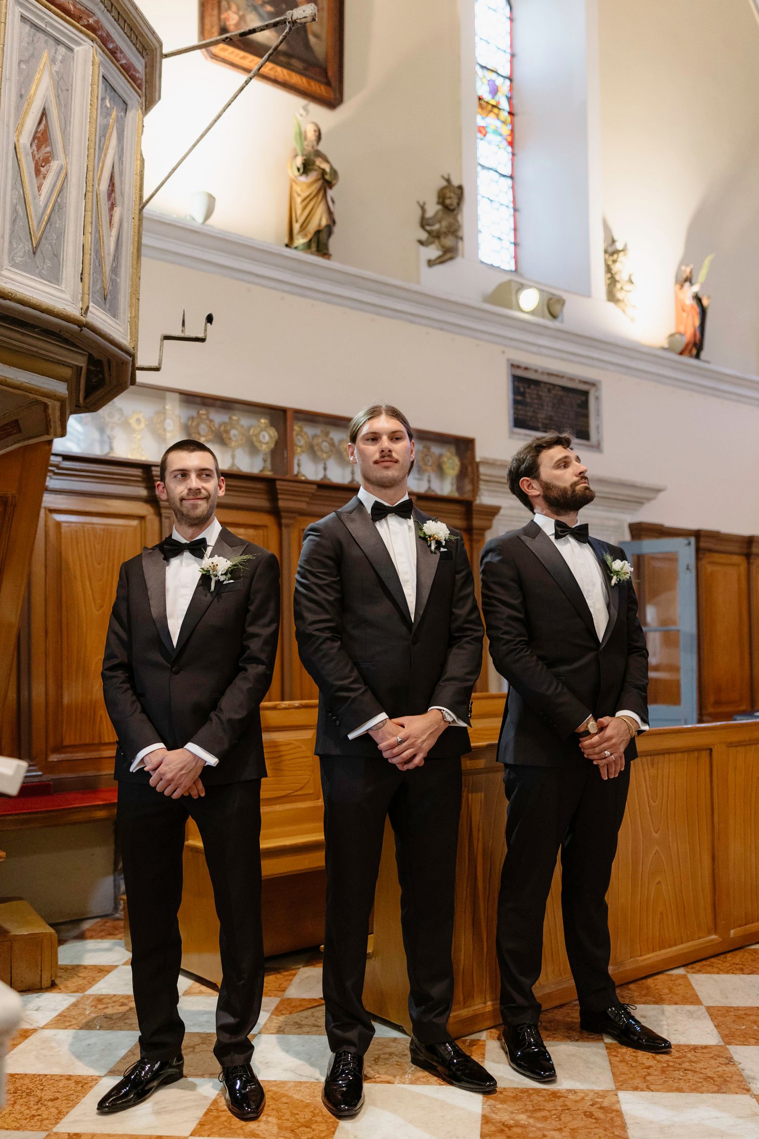 Groomsmen in black tuxedos seated in church pews for formal wedding photo.