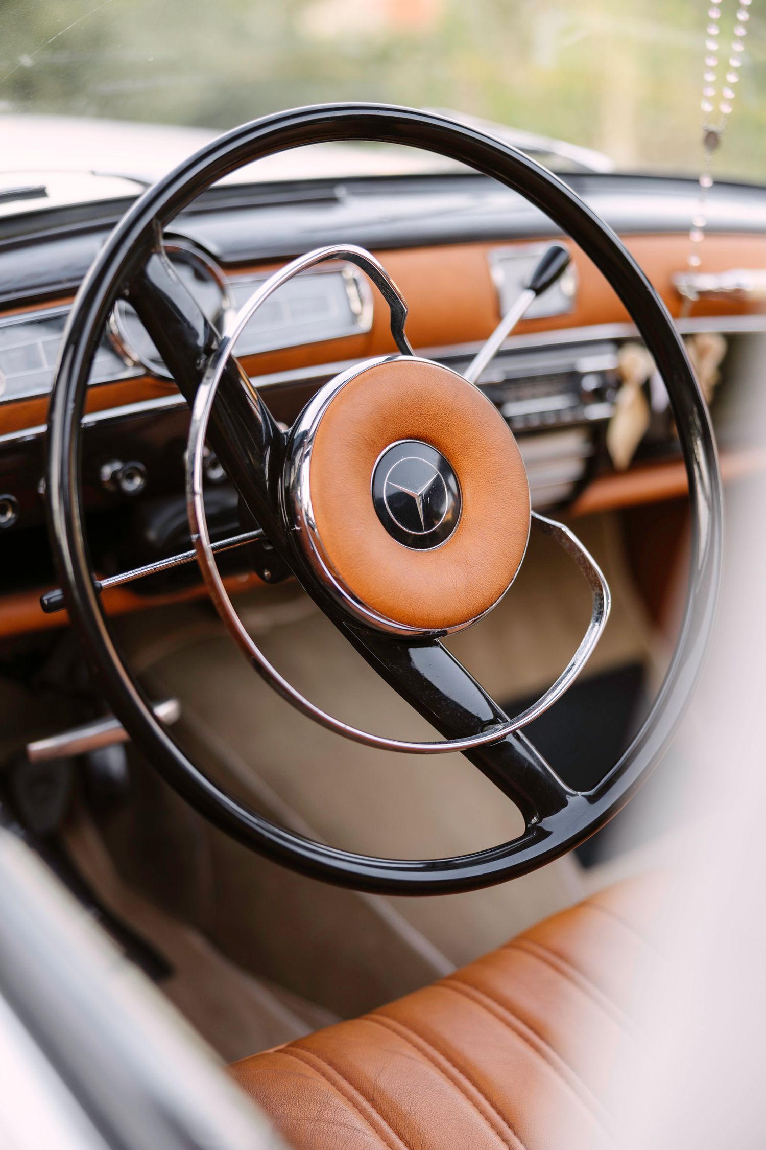Vintage car dashboard with brown leather seats and classic black steering wheel.