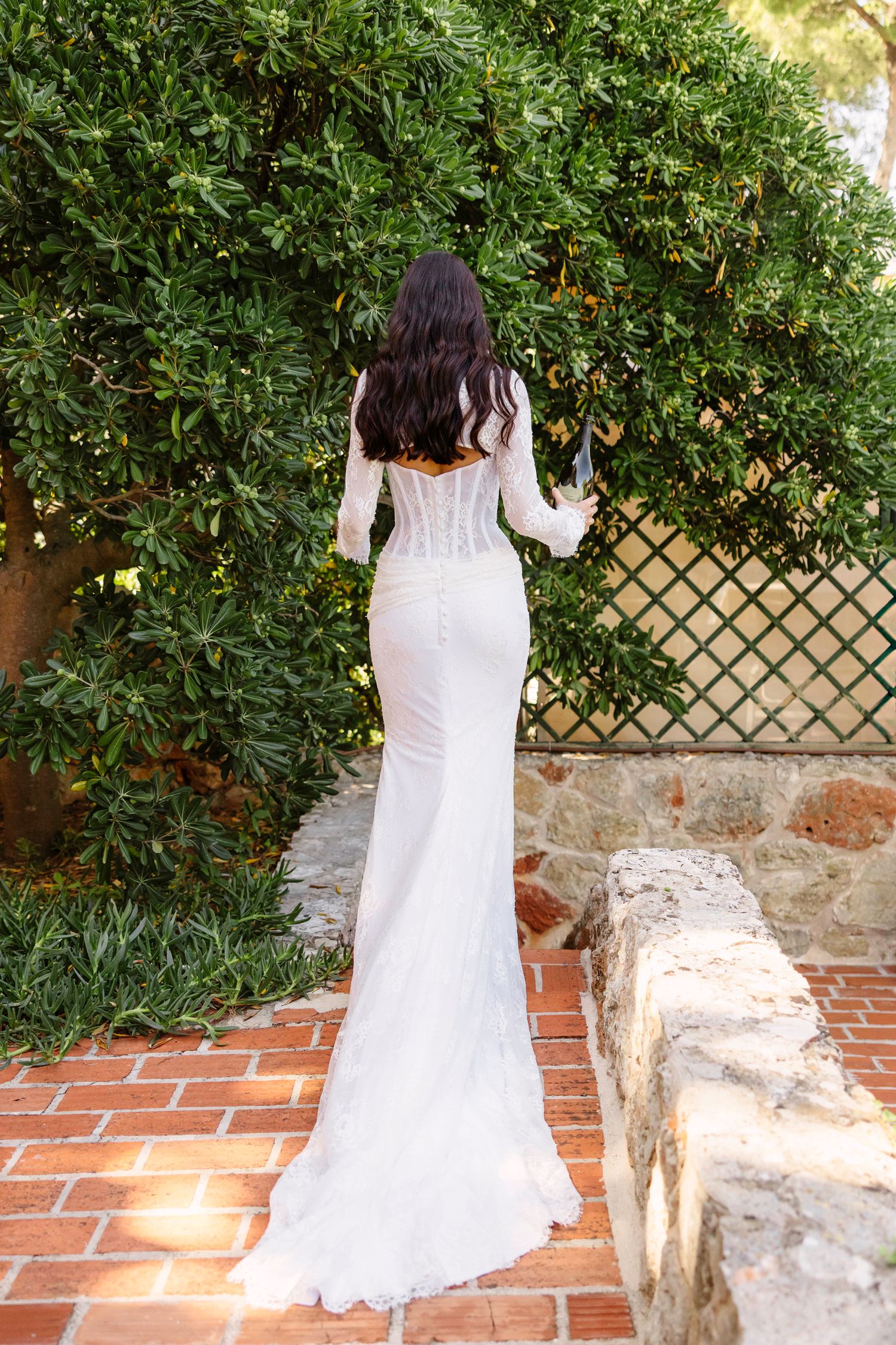 Back view of a flowing white wedding dress with lace details in an outdoor garden setting.