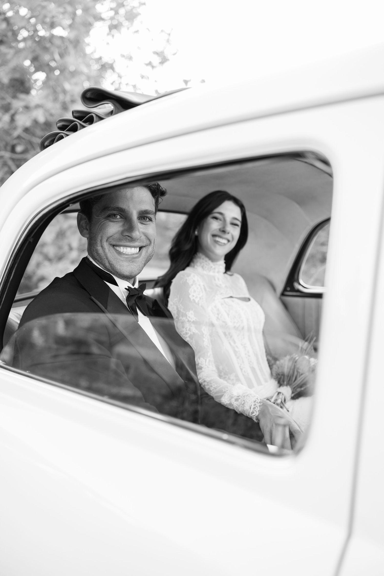 Happy newlyweds smile while sitting in a classic white wedding car. Hvar, Croatia.