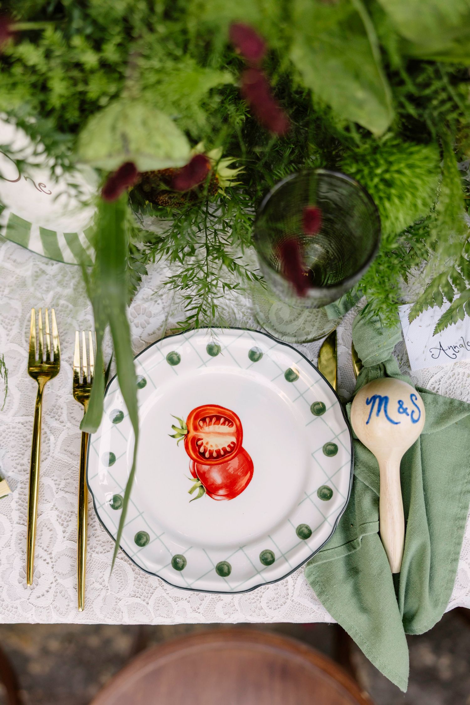 Wedding table settings with gold cutlery, painted plates, and green botanical decorations. Hvar, Croatia