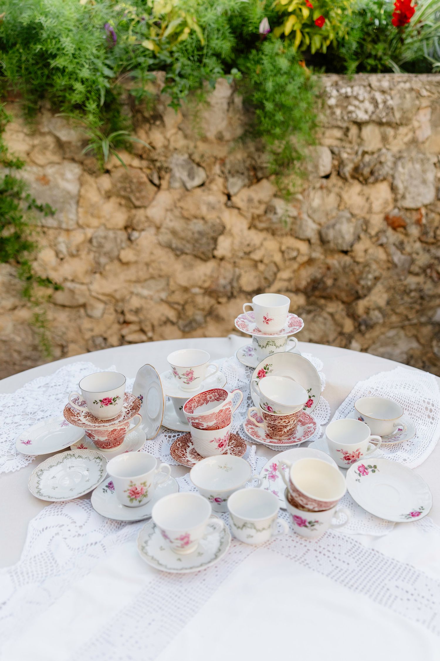 Collection of vintage floral teacups and saucers arranged on white lace tablecloth.