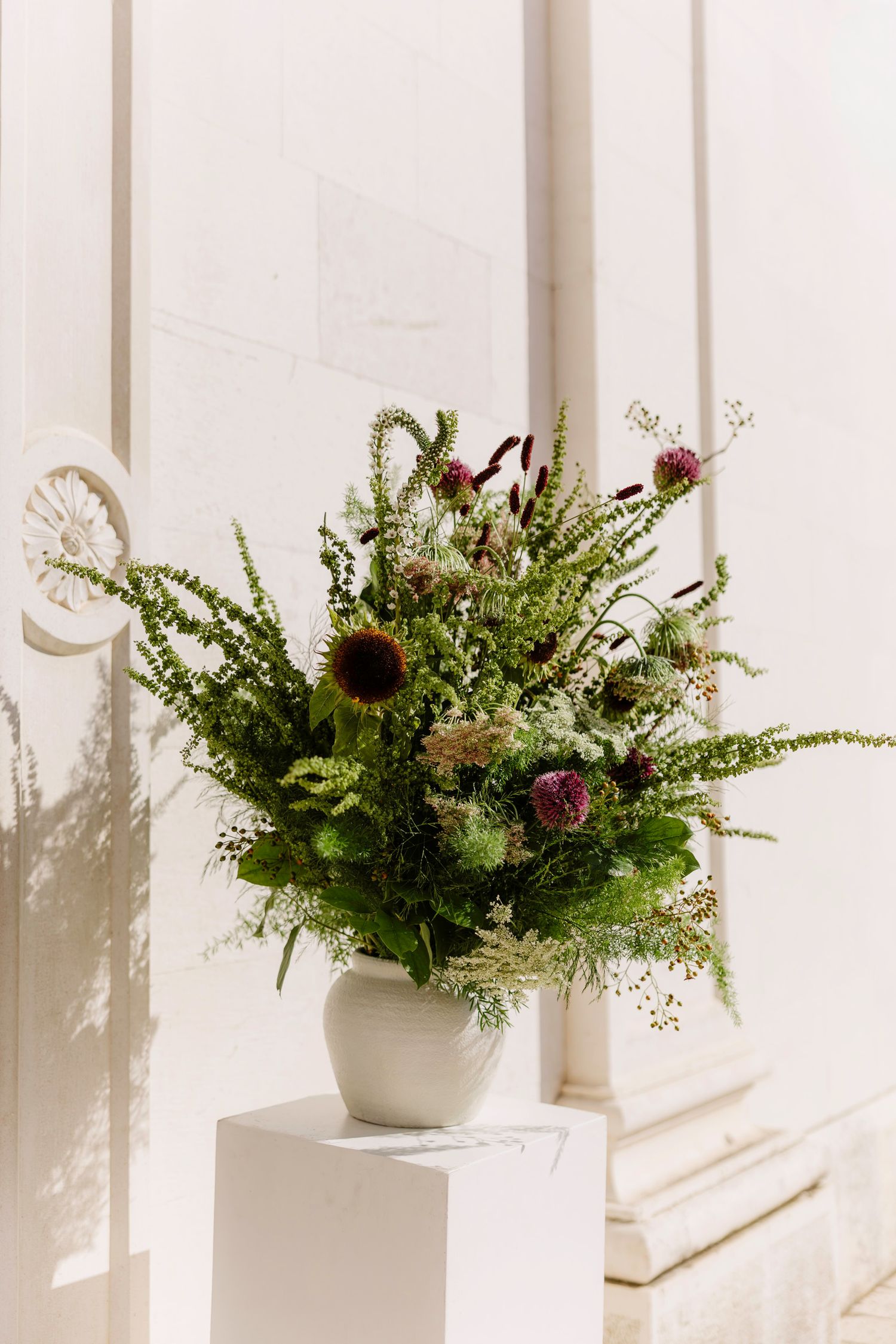 Row of lush greenery and floral arrangements displayed against a white wall.