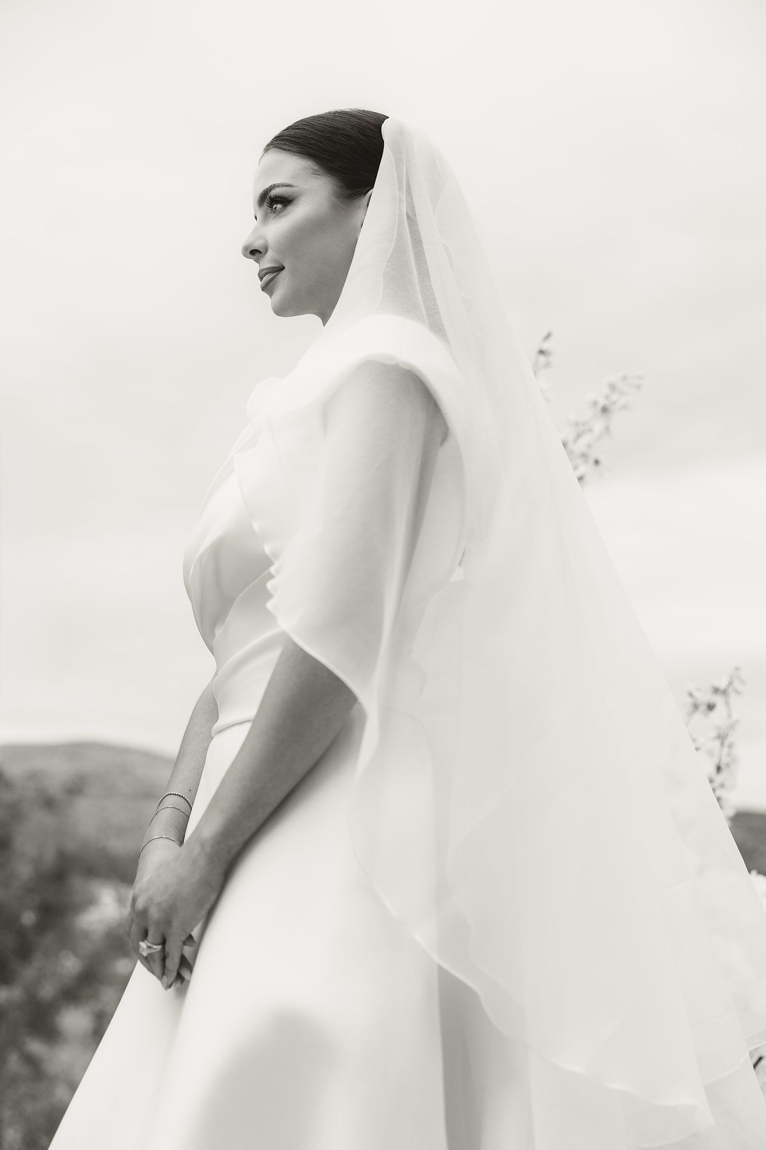 A bride in a classic white wedding dress and veil poses elegantly in a series of soft, ethereal black and white photos.