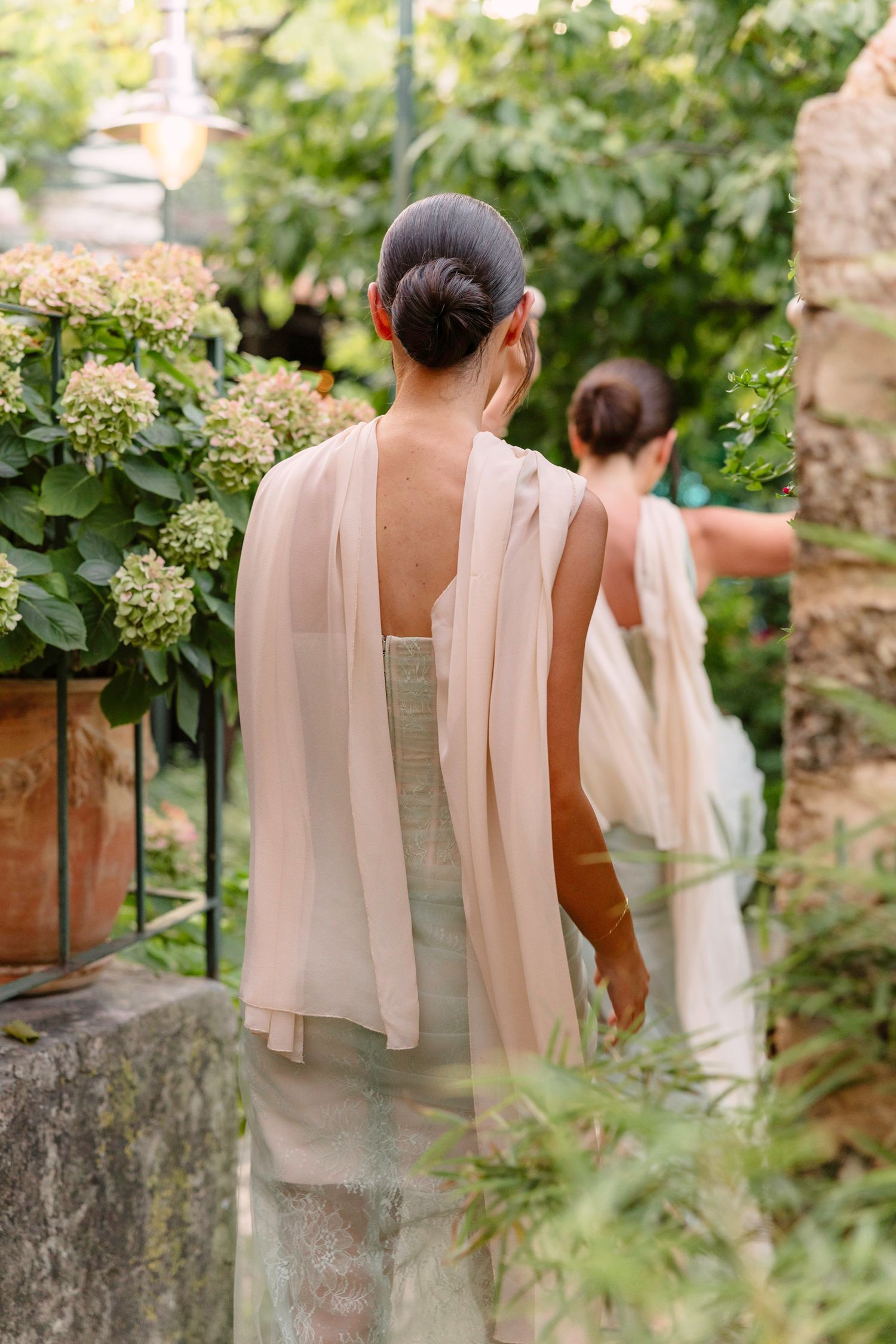 Elegant bridesmaid in a mint dress with flowing shawl walks through a garden setting. Hvar, Croatia
