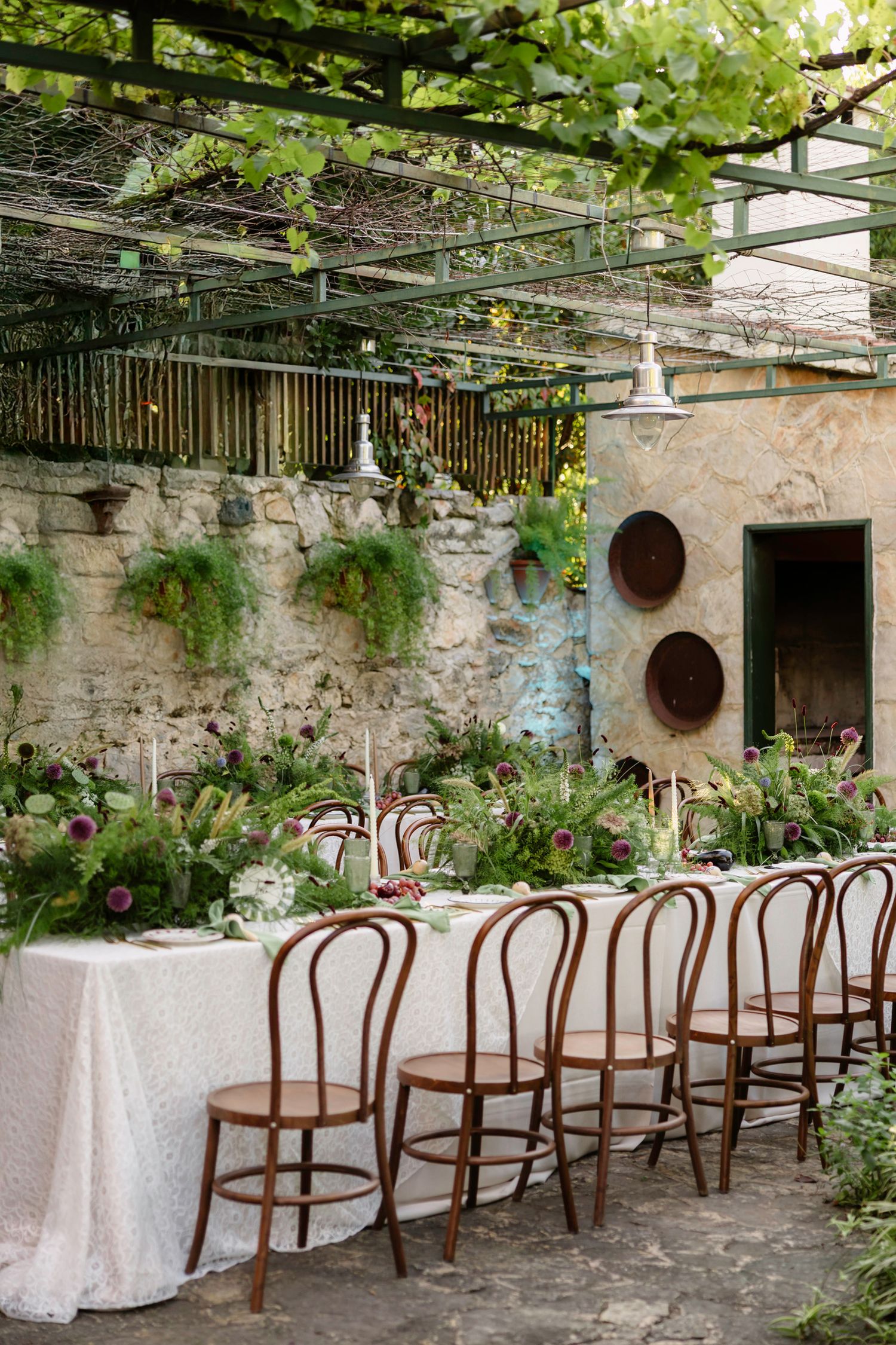 Stone-walled outdoor dining space with wooden chairs arranged under a vine-covered pergola. Hvar, Croatia