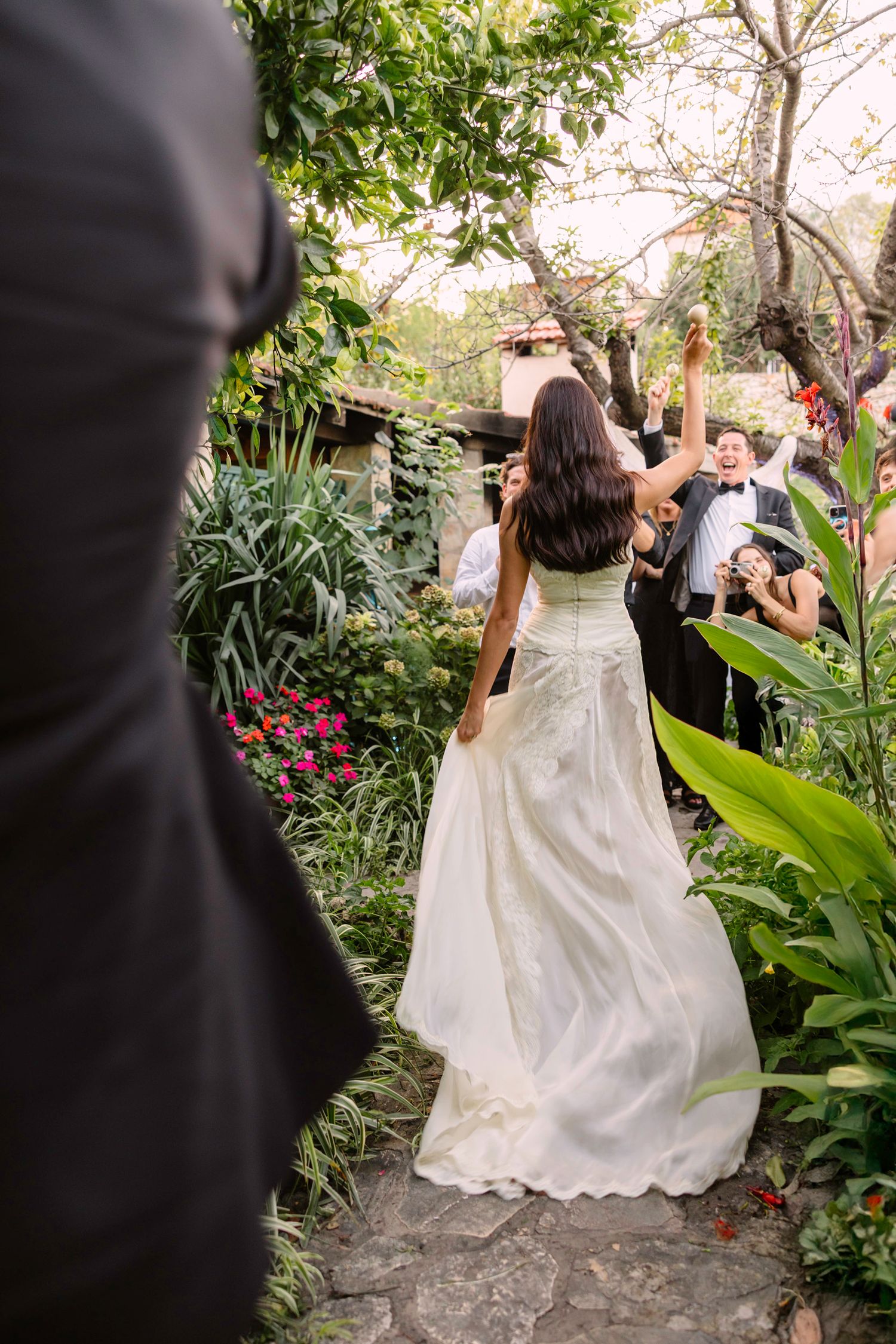 A bride in flowing white gown walks through a lush garden pathway during wedding celebrations. Hvar, Croatia