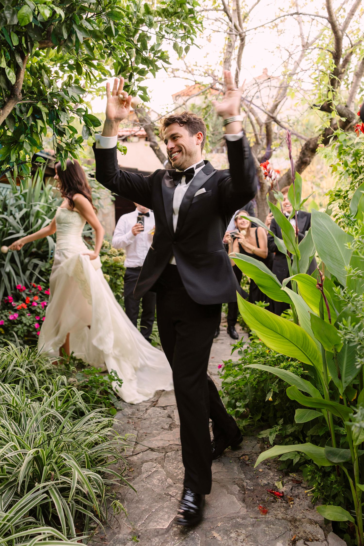 Wedding guest celebrates with raised arms on garden path surrounded by tropical plants and flowers. Hvar, Croatia