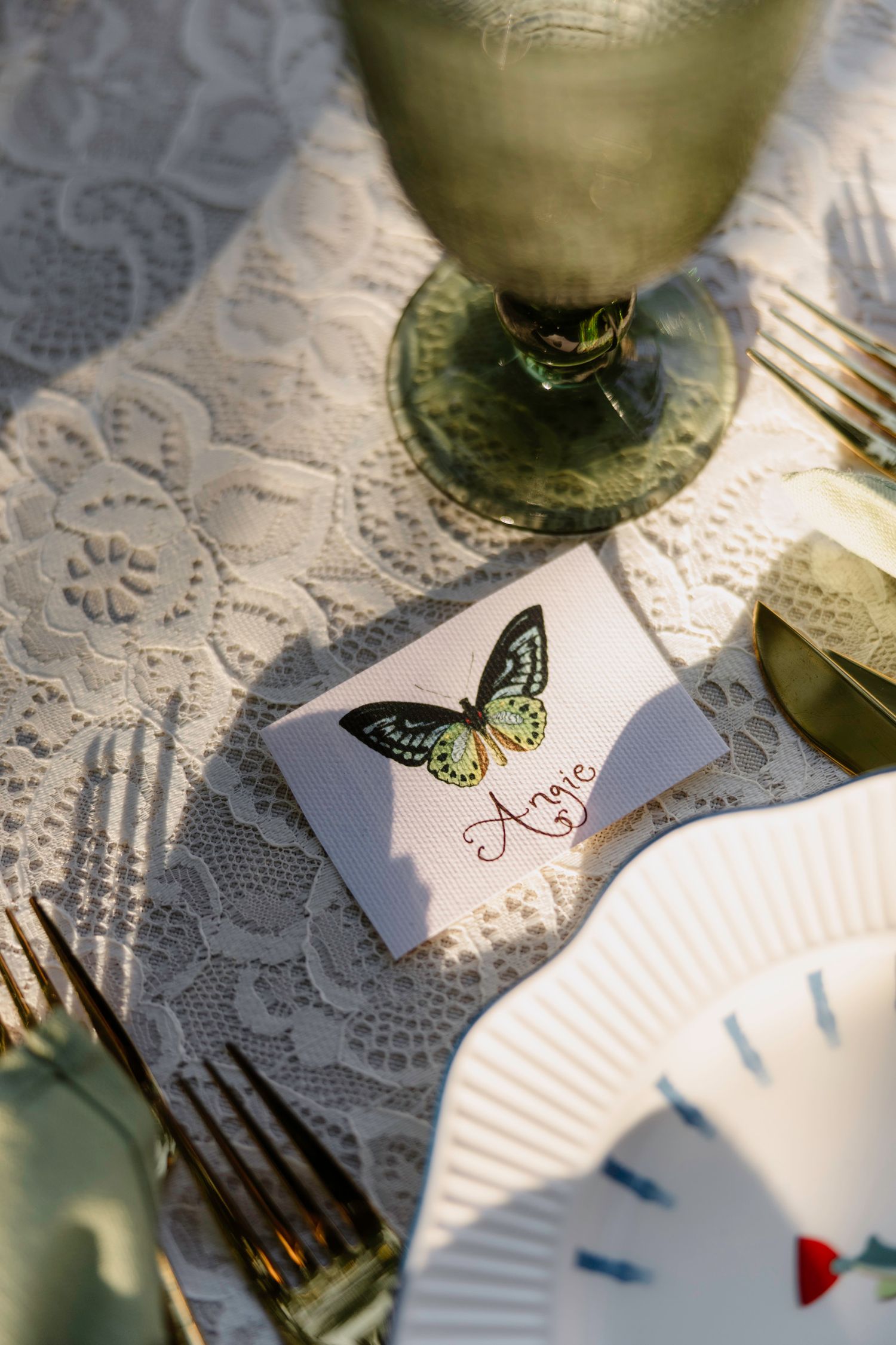 Delicate butterfly place card on white lace tablecloth next to glassware at an elegant table setting. Hvar, Croatia