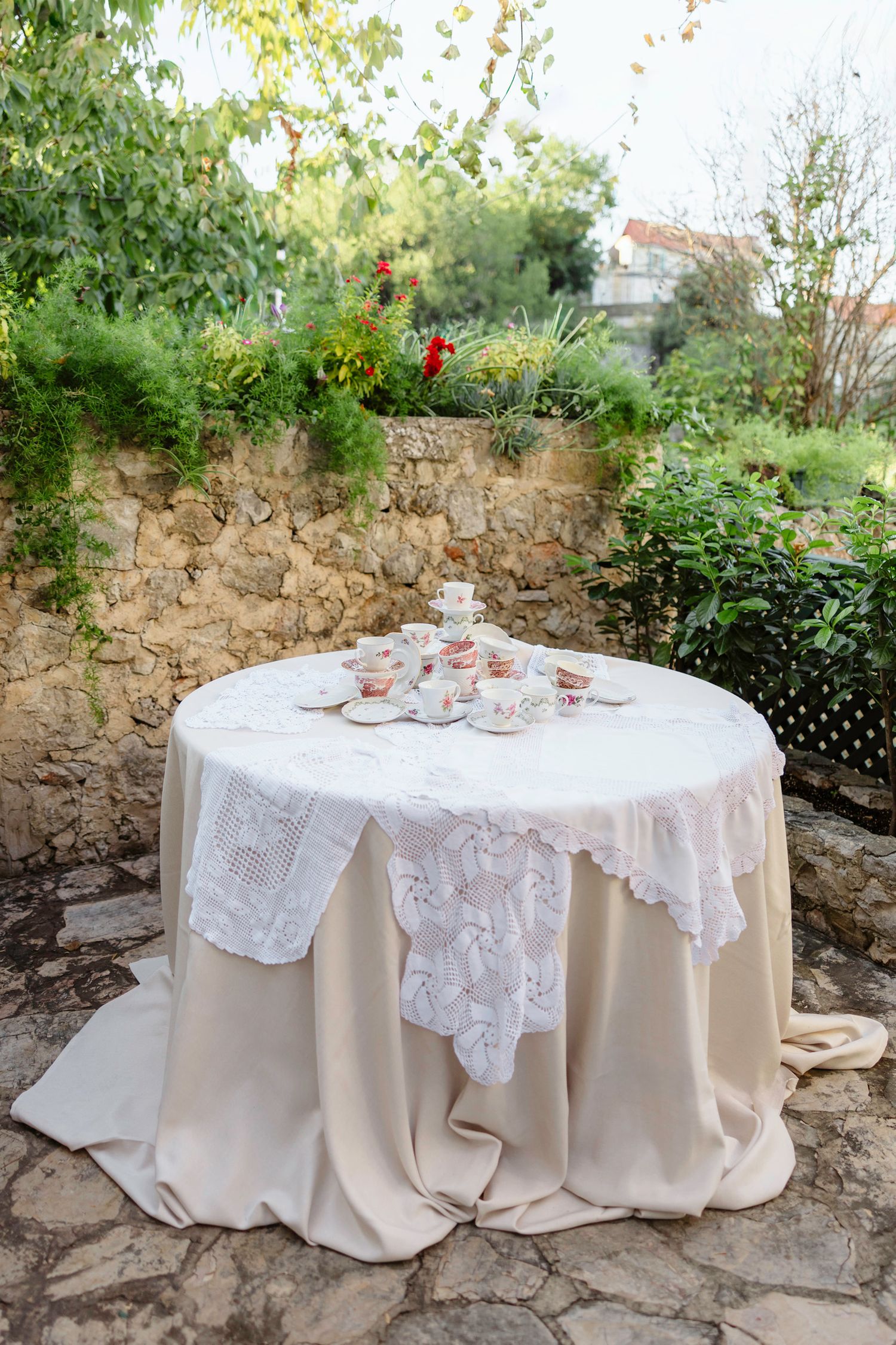 Round table with layered white lace tablecloth and beige underlay in an outdoor garden setting. Hvar, Croatia