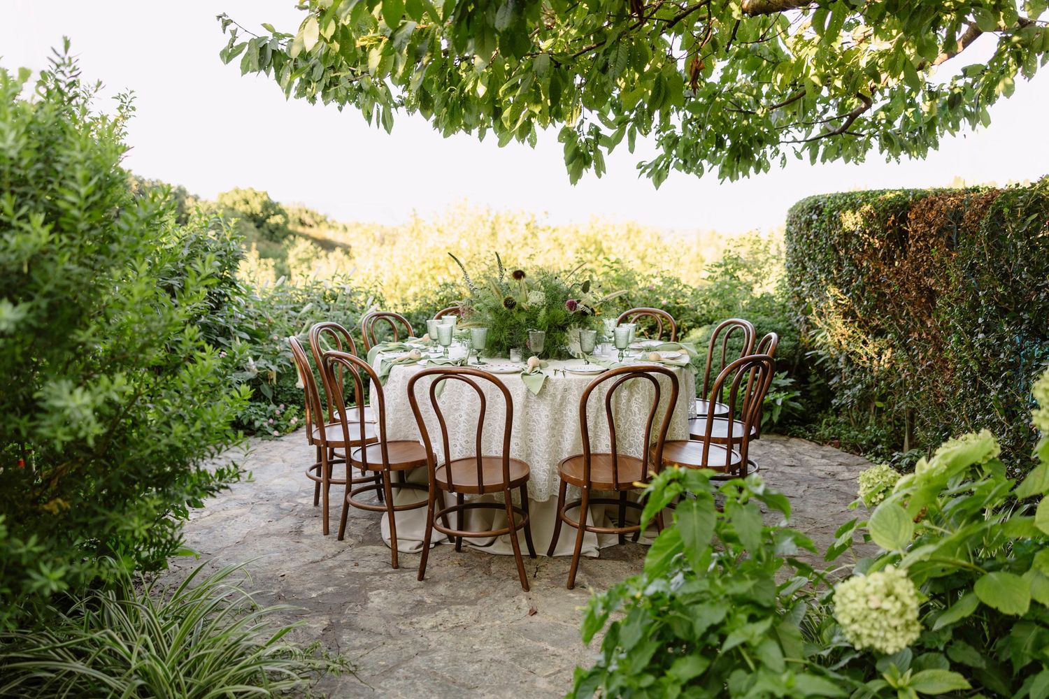 Garden dining area set under lush green trees with wooden chairs arranged for an outdoor event. Hvar, Croatia