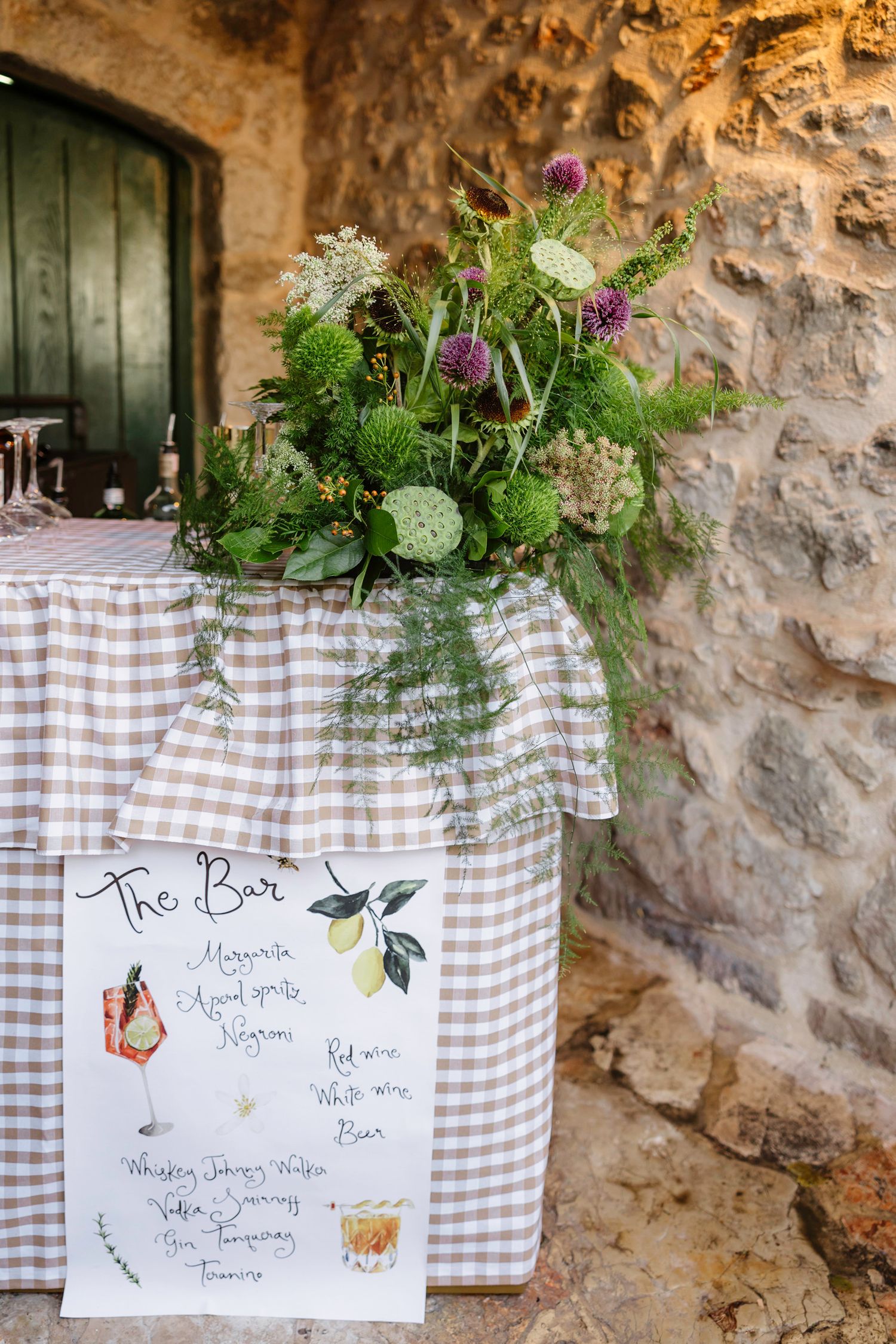 Rustic bar menu signs decorated with greenery against stone wall.