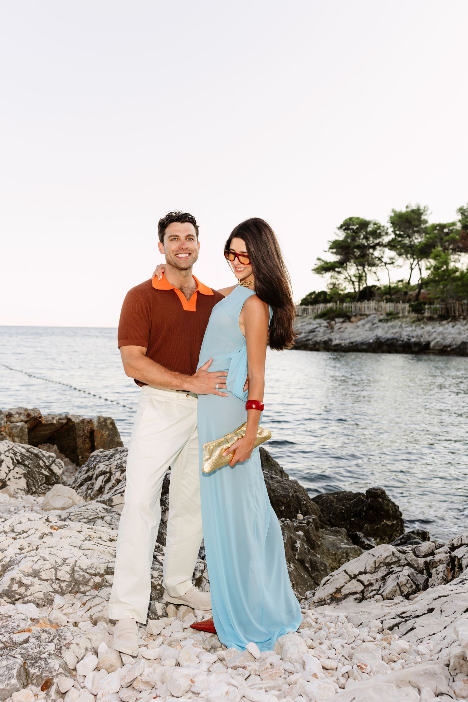 Couple enjoying sunset on rocky beach shore in casual attire.